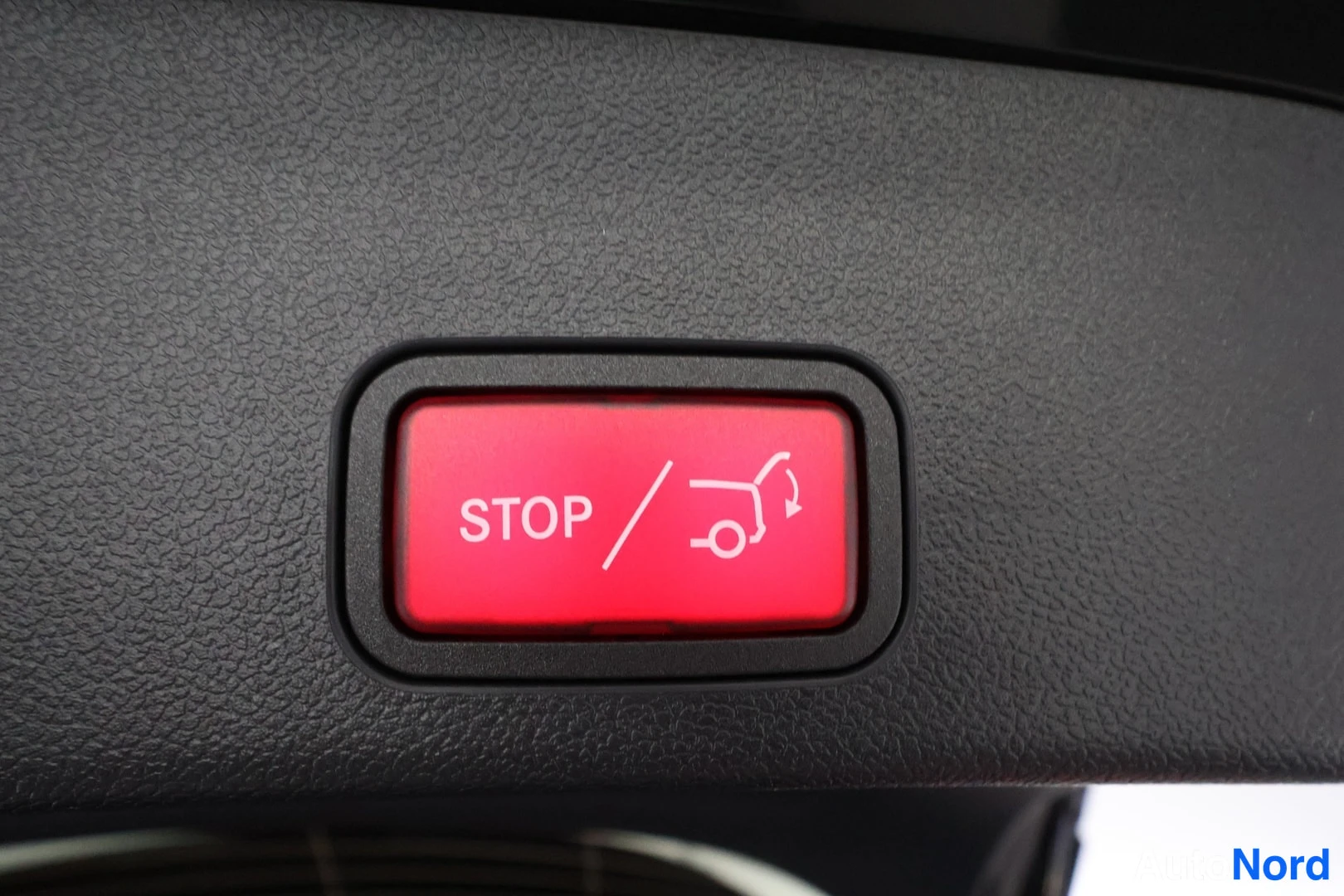 Yksityiskohta: Punainen POWER LIFTGATE -painike, teksti STOP ja sulkuvipu-ikoni tummassa sisäpaneelissa.