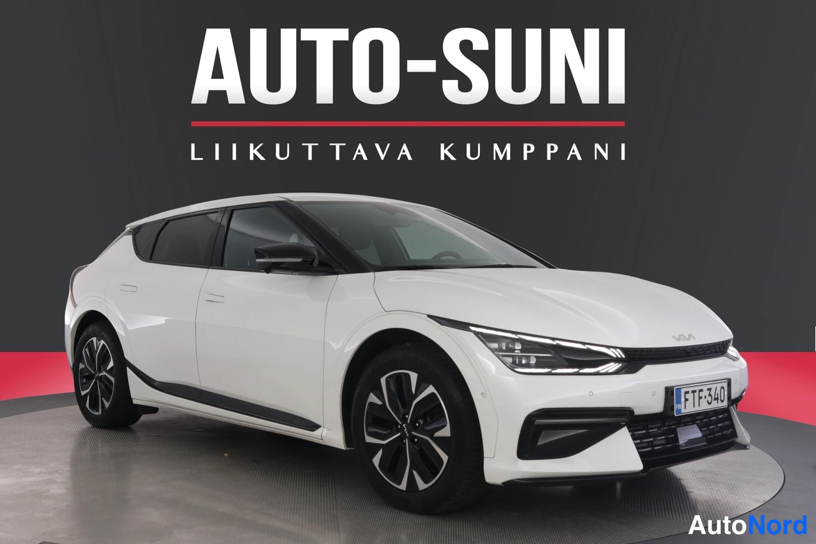Etuviisto, nokka oikealle: Kia EV6 edestä vasemmalta kuvattuna, valkoinen crossover tummassa studiossa.