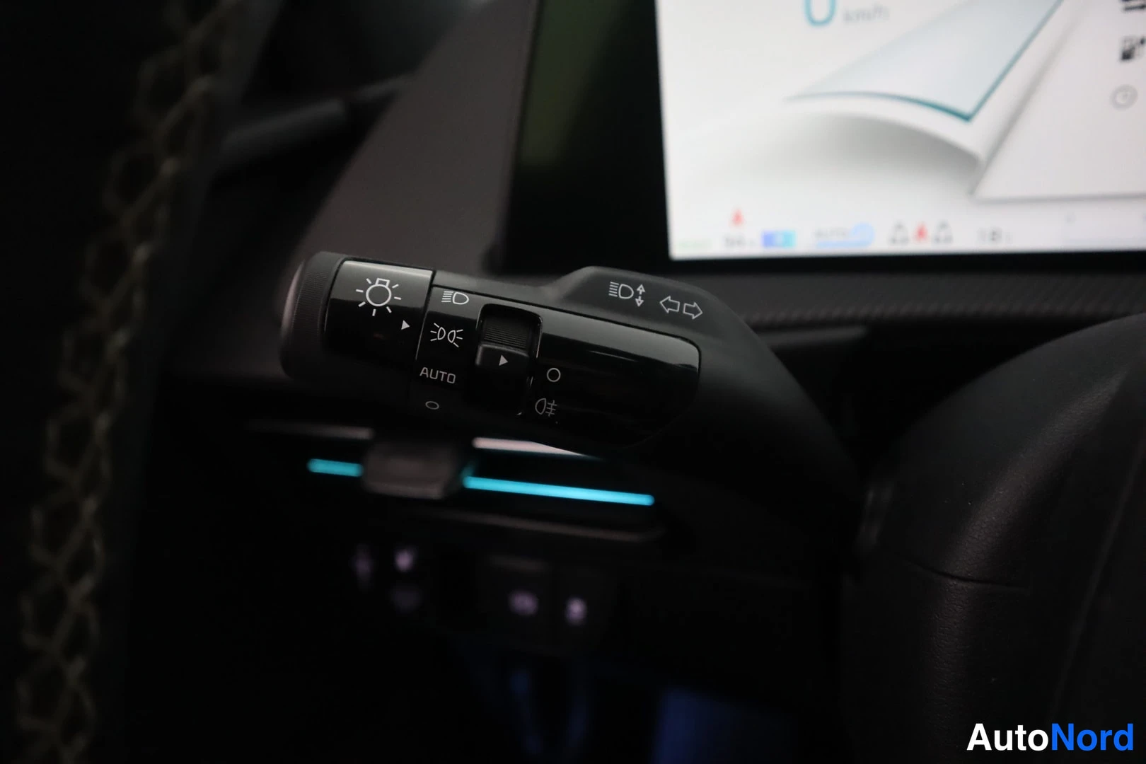 Yksityiskohta: Sisätilakuvan valon ja suuntavilkun vipu, jossa AUTO-merkintä ja instrumenttinäytön reuna taustalla.