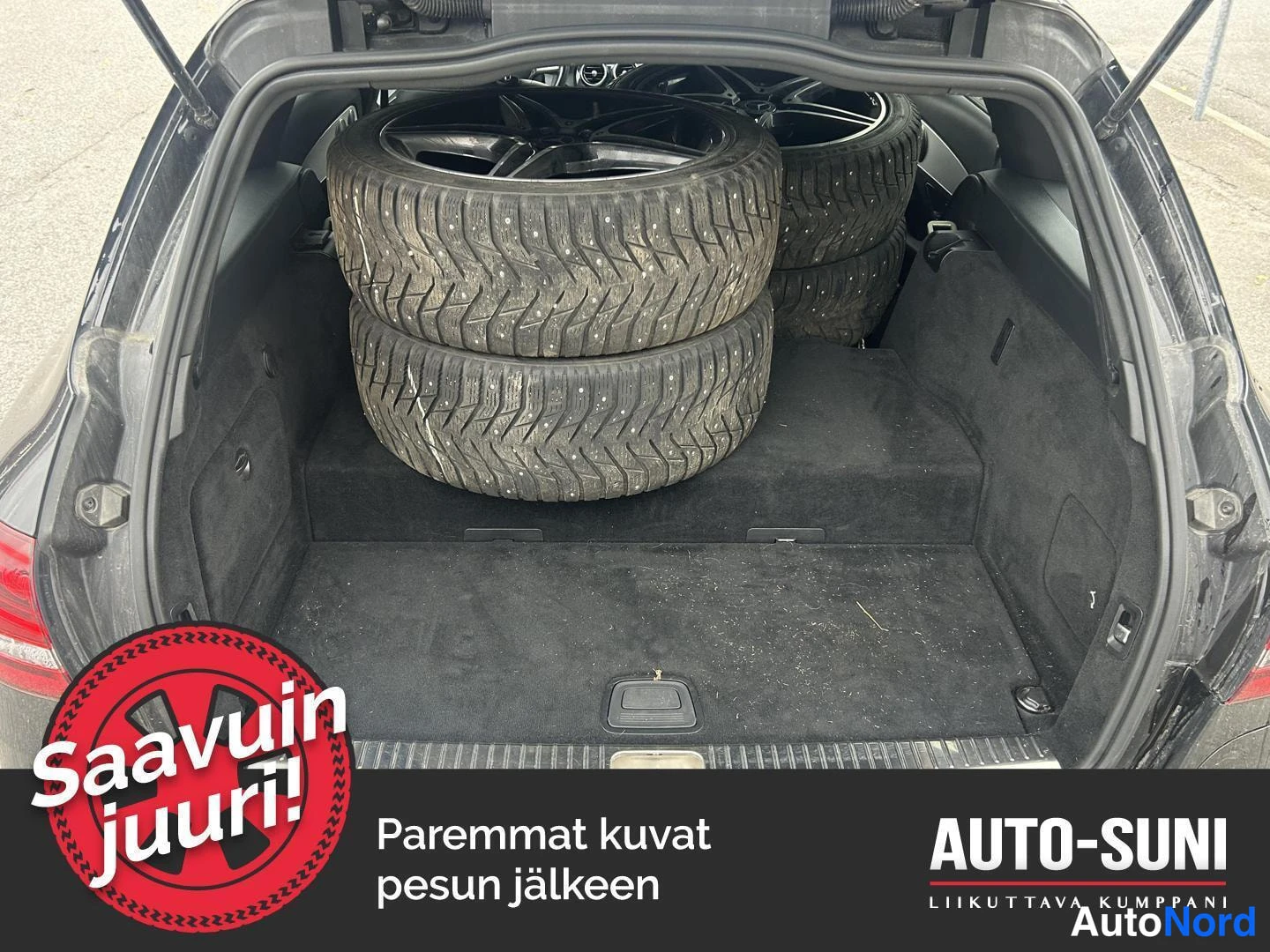 Takaa: Auton takaluukku auki; tavaratilassa neljä karhennettua kitkarengasta vanteilla pinottuna, musta matto lattialla.