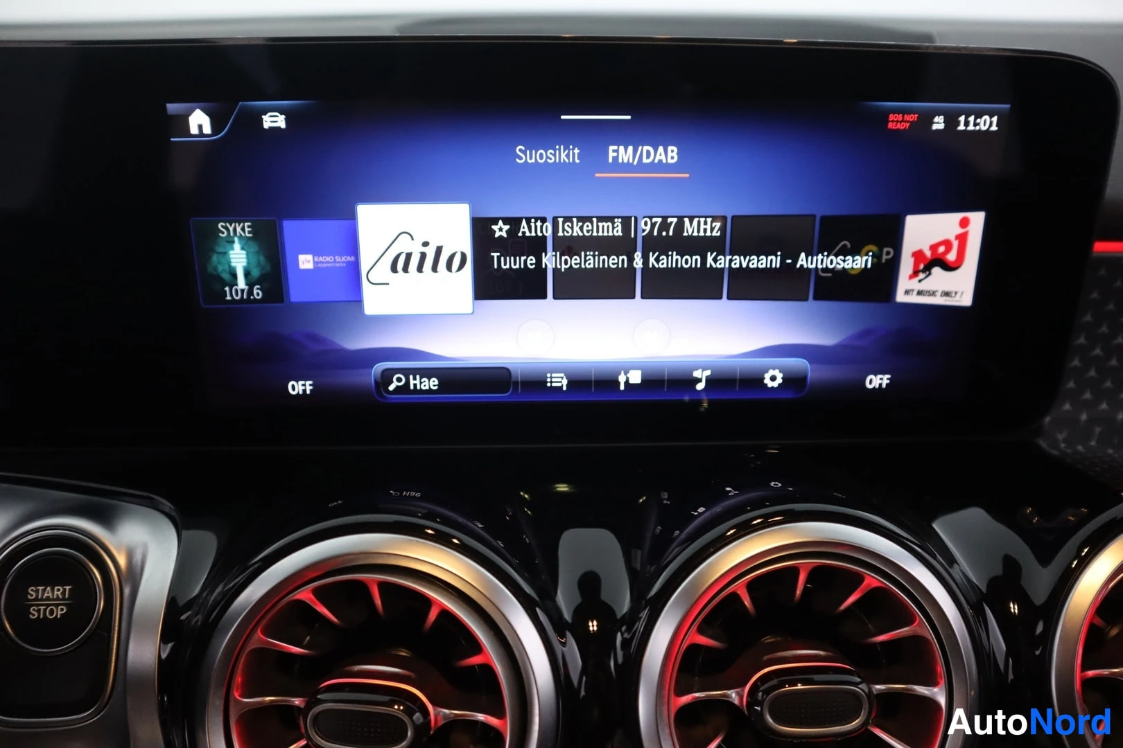Muu: Infotainment-näytön FM/DAB-radiokanavalista suosikeilla, muun muassa Aito Iselmä 97,7 MHz; näytön alla pyöreät ilmastointisuuttimet ja Start Stop -painike.