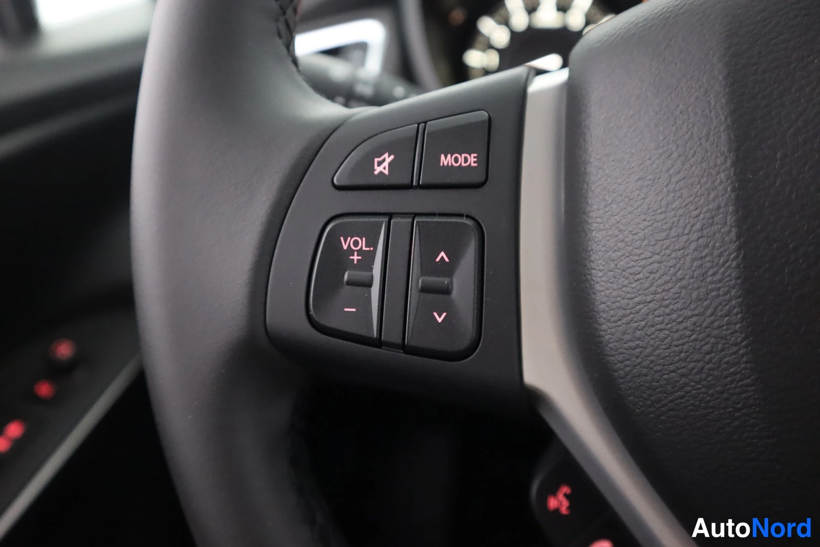 Muu: Suzuki S-Cross ohjauspyörän vasen kytkinryhmä lähikuvassa, VOL.- ja MODE-painikkeet punaisin merkinnöin.