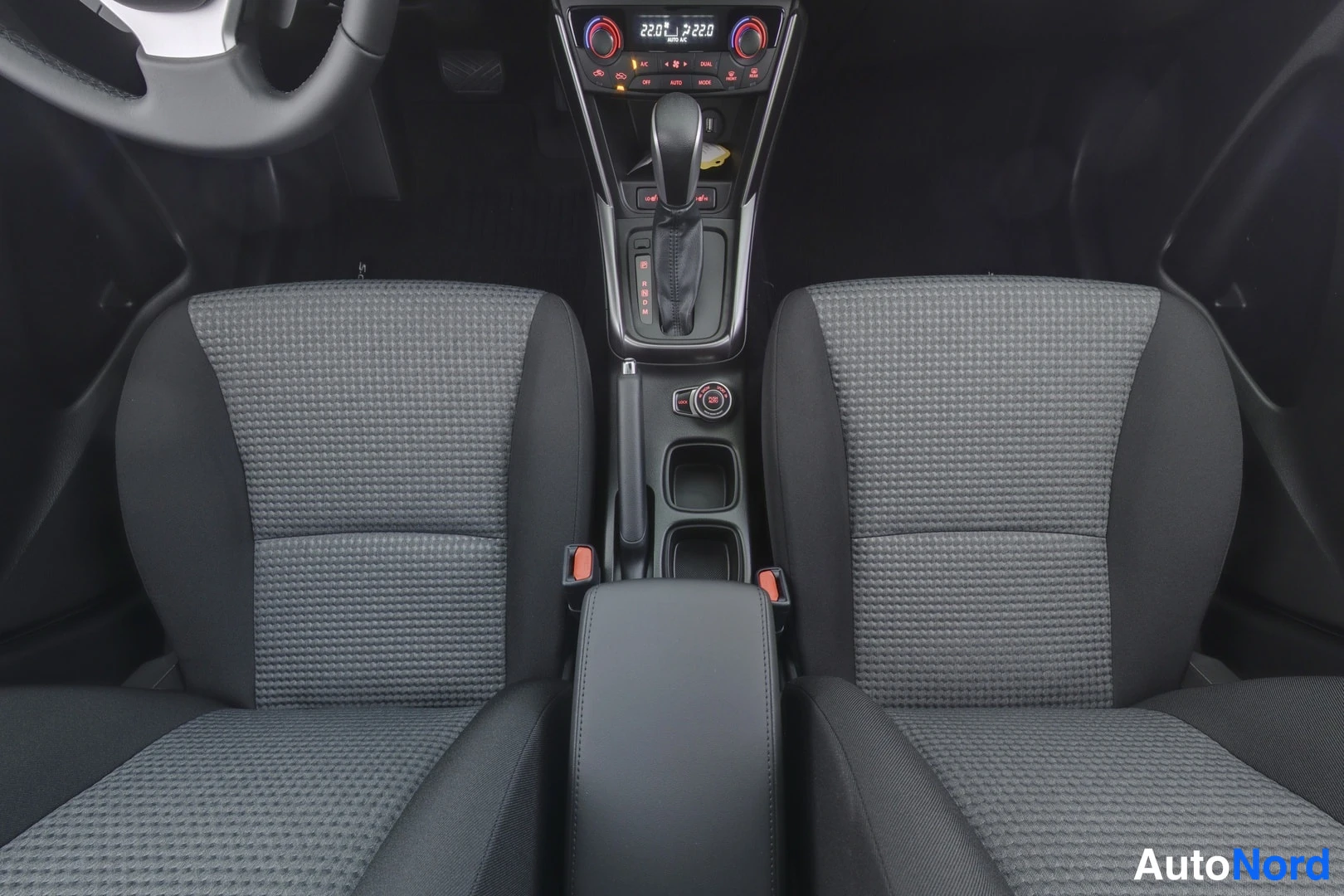 Etuistuimet: Interior shot from above showing two front seats with grey patterned fabric upholstery, a centre console with automatic gear lever, handbrake and cupholders, pa