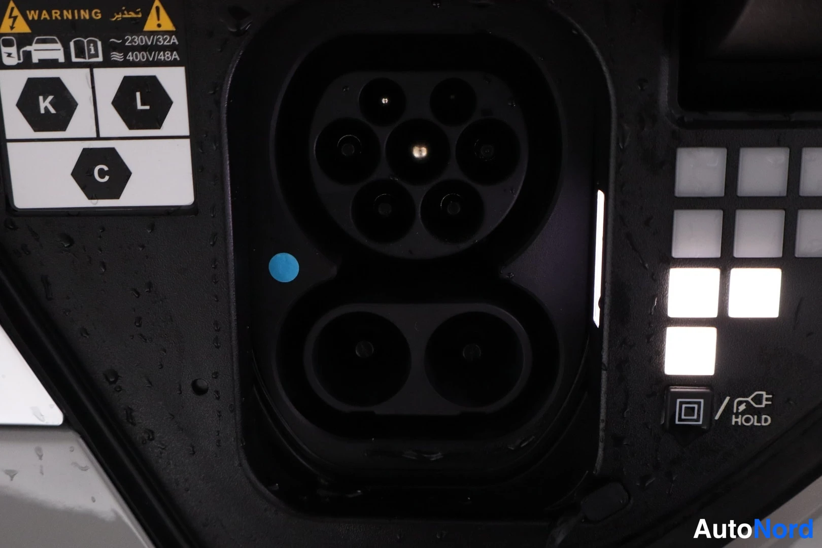 Yksityiskohta: Sähköauton latausliitin auki: ylhäällä Type 2 -pistoke ja alhaalla DC-pistokkeet, vieressä valaistut painikkeet ja HOLD-merkintä. Tarra ilmoittaa 230V/32A ja 40