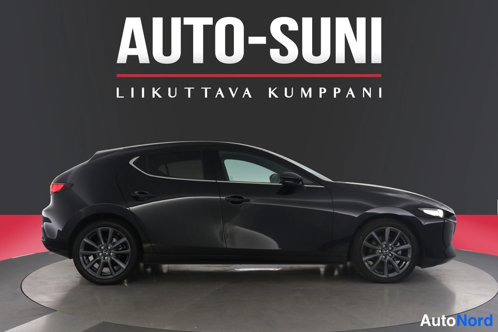 Sivulta: Mustan Mazda 3:n sivuprofiili studiotunnelmassa, AUTU-SUNI-banneri taustalla.