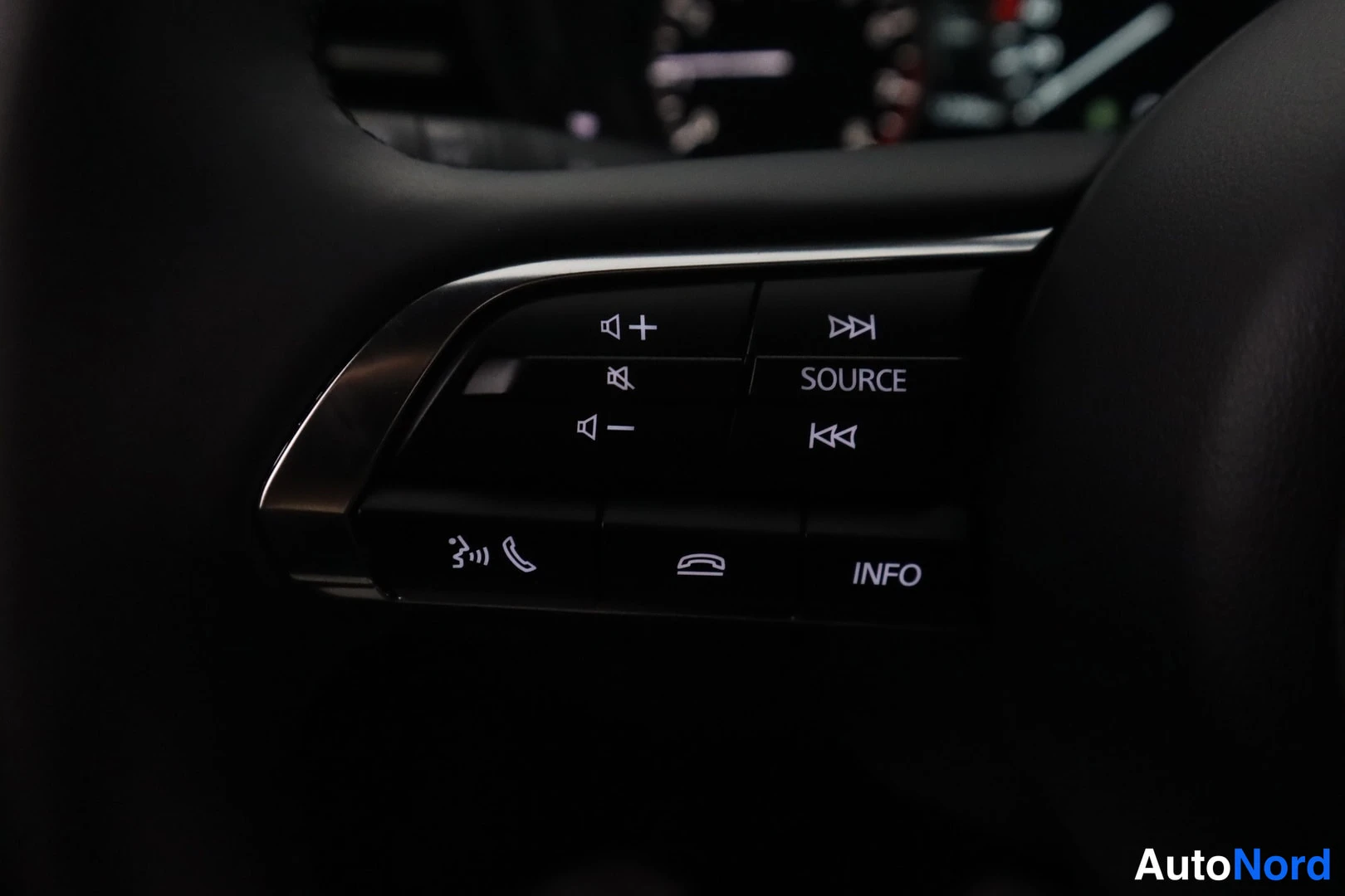 Yksityiskohta: Close-up view of the right-hand side of a steering wheel showing control buttons for audio, including volume plus and minus, track skip forward and back, source