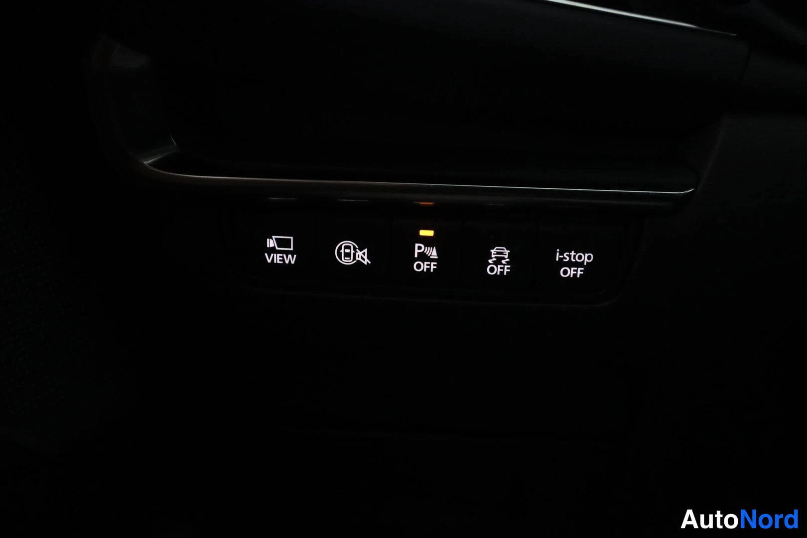 Yksityiskohta: Dashboard console panel showing a row of buttons with icons and text: VIEW (with a camera symbol), traction control OFF with an illuminated light above it, stab