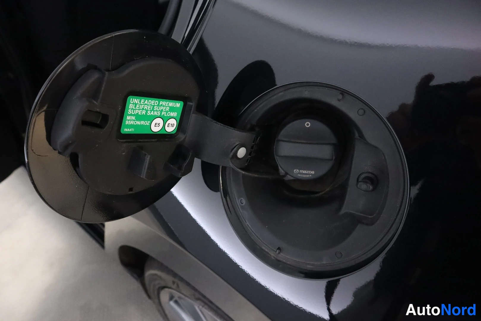 Muu: Auki käännetty tankkiluukku ja polttoainesäiliön tulppa; tarra lukee UNLEADED PREMIUM, E5 ja E10, 95RON/ROZ.