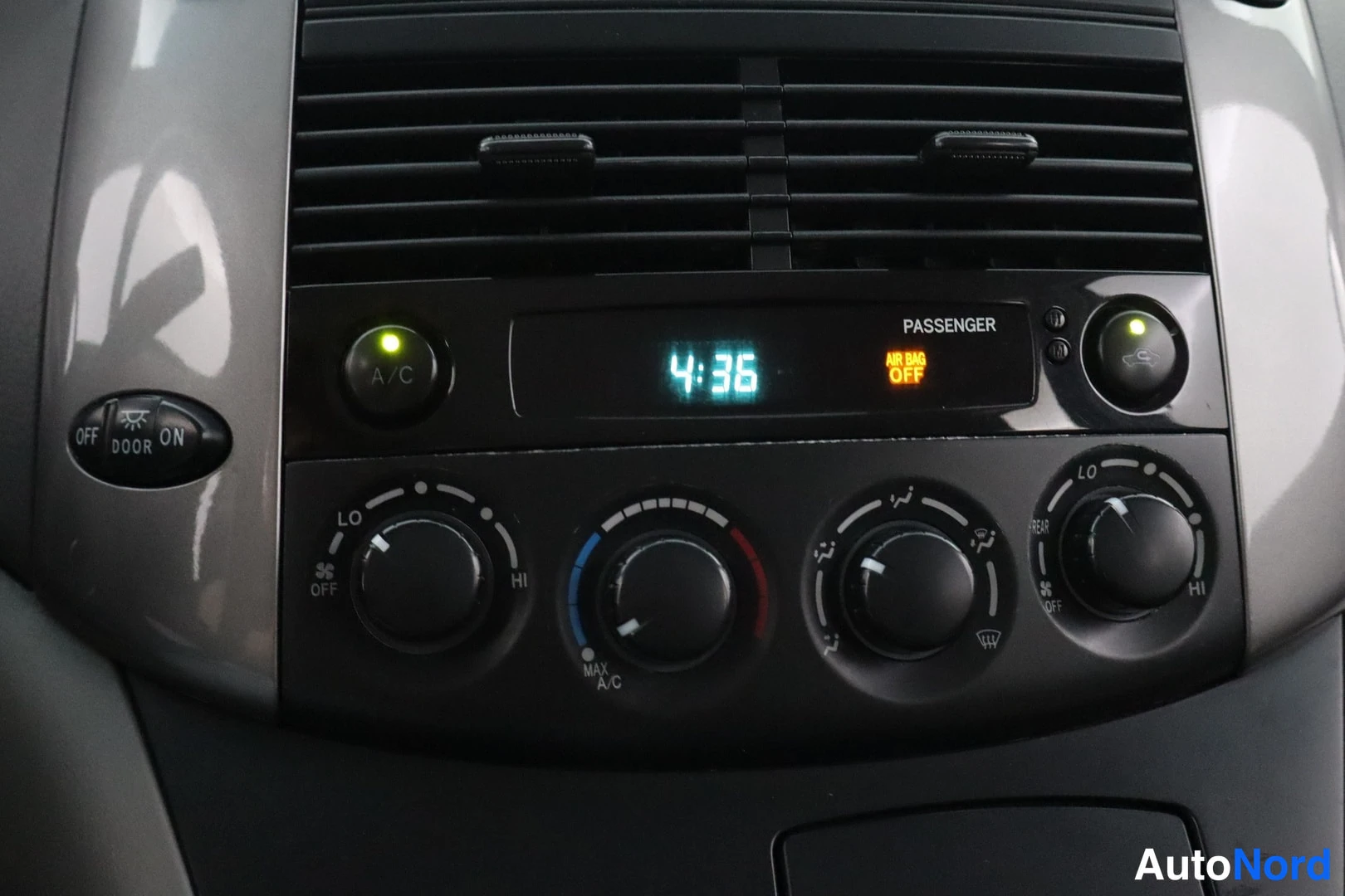 Muu: Toyota Sienna -kohdekuva 2: lähikuva ilmastointipaneelista; näytössä kello 4:36 ja PASSANGER AIR BAG OFF -merkki, A/C-painike palaa vihreänä, neljä säätönuppia