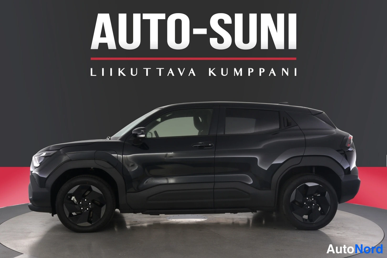 Sivulta: Musta SUV:n sivuprofiili studiotaululla, jossa AUTO-SUNI-mainoskuvitus ja punainen pohjaympyrä.