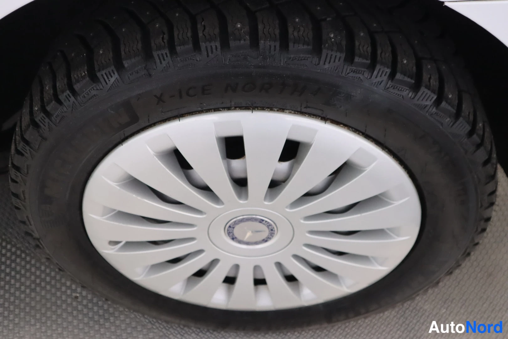 Yksityiskohta: Lähikuva auton pyörästä: hopea Mercedes-pölykate ja musta kitkarengas, jonka sivussa lukee X-ICE NORTH 4.