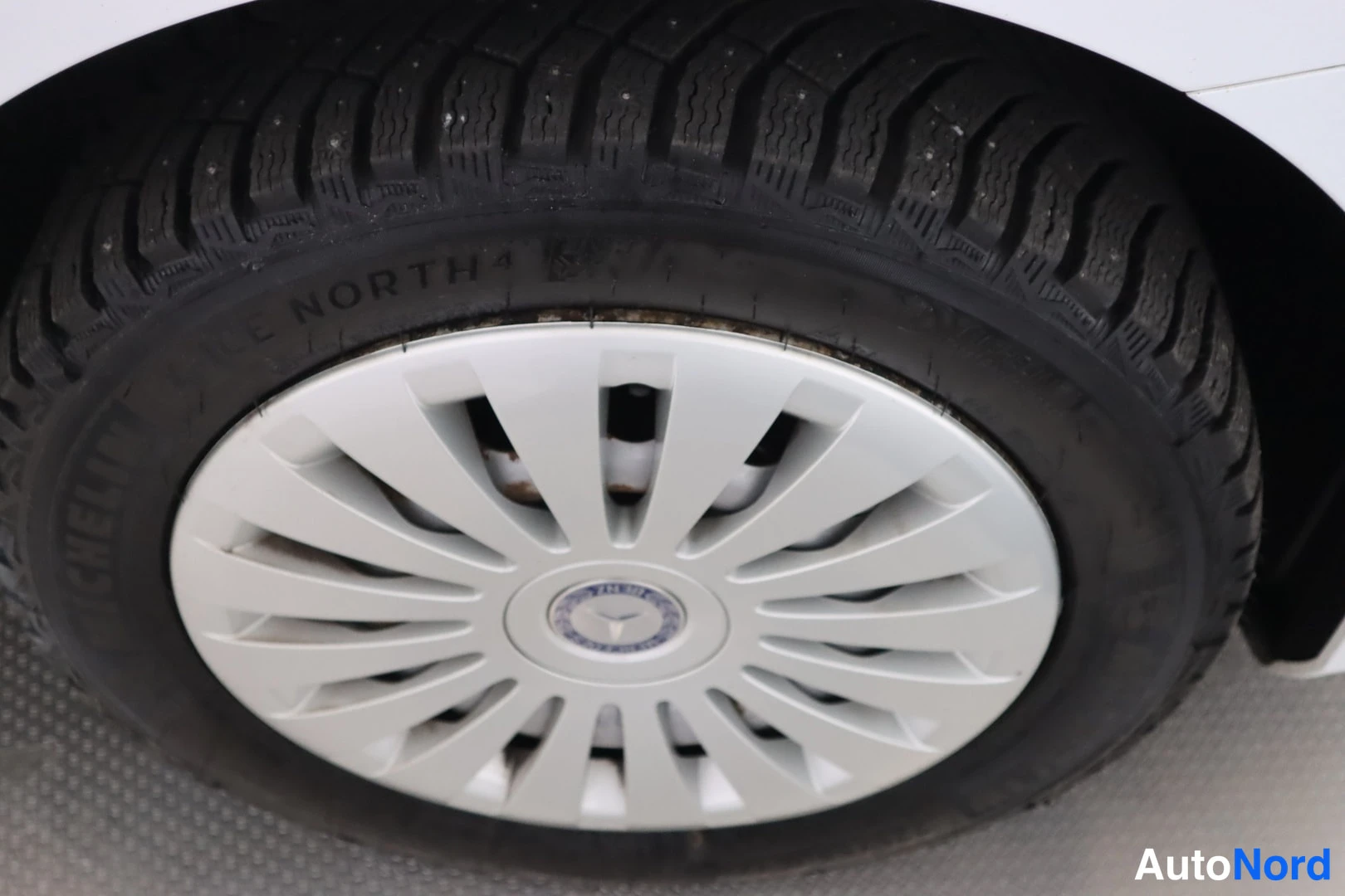 Yksityiskohta: Lähikuva auton pyörästä: hopea Mercedes-pölykate, mustan renkaan sivussa lukee NORTH 4 ja MICHELIN.