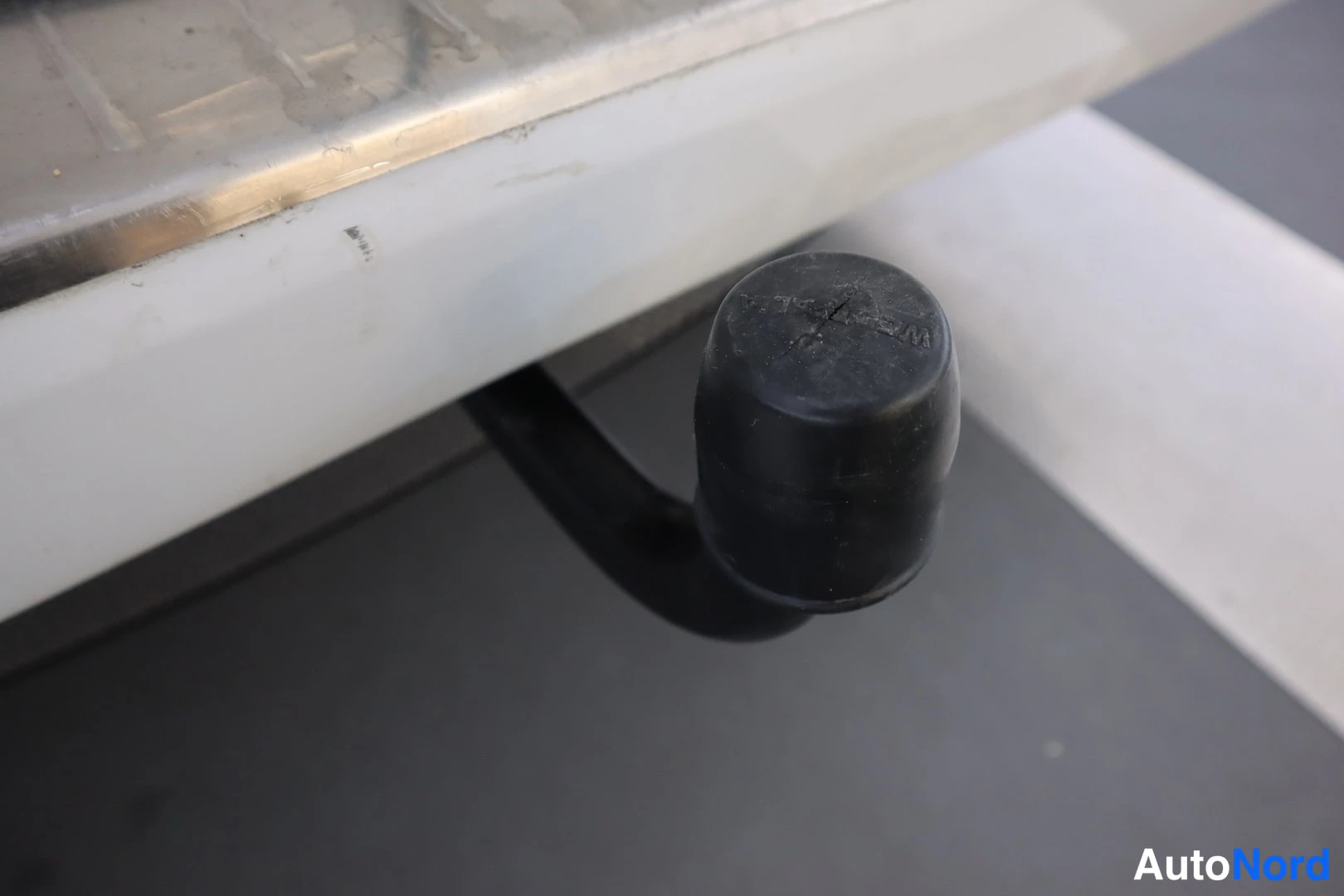 Yksityiskohta: musta Westfalia-kytkinkansipeite takapuskurin alla, valkoinen puskuri ja metallinen lastauskynnys.