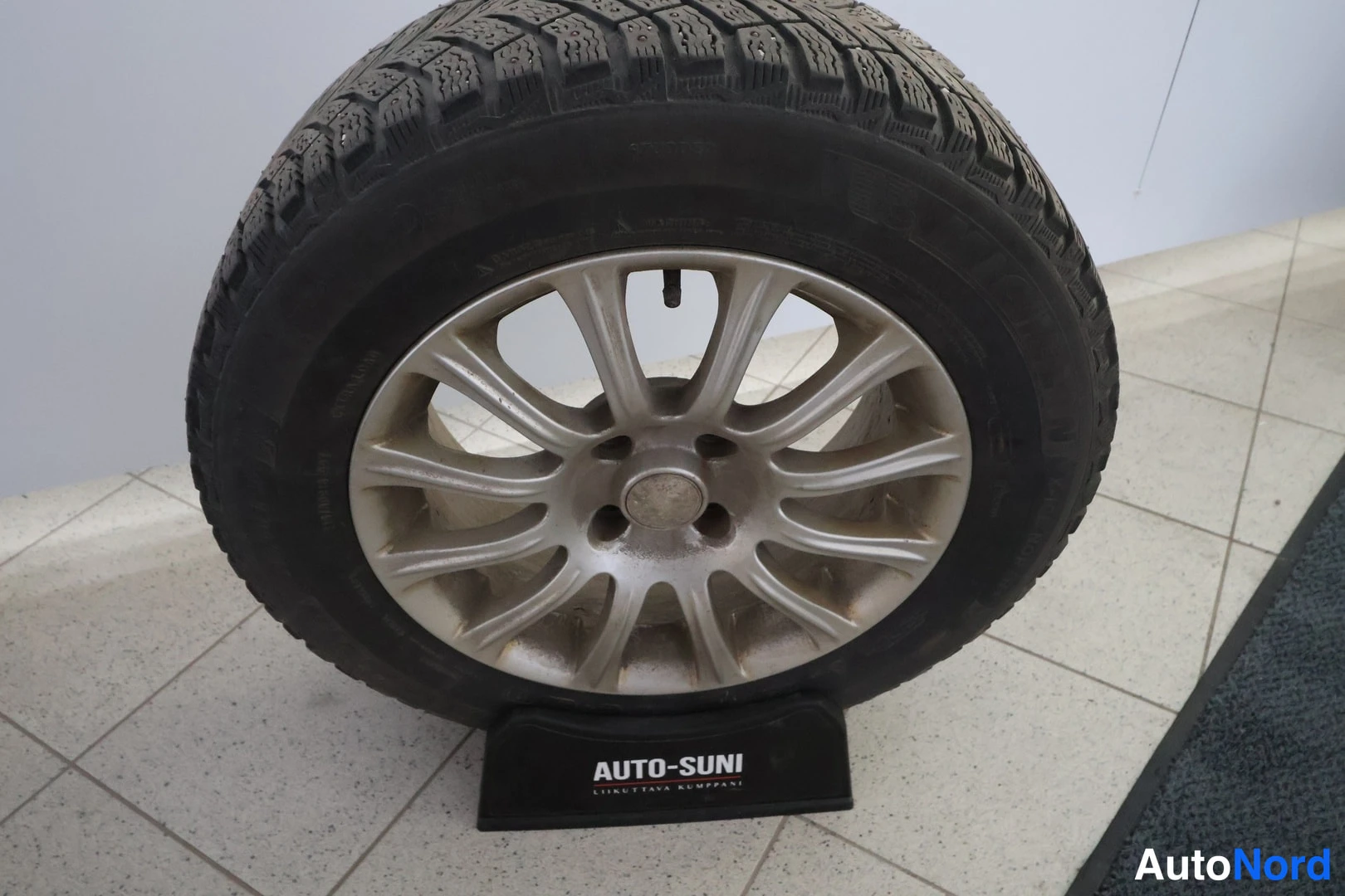 Yksityiskohta: Irrotettu rengas alumiinivanteella AUTO-SUNI-telineessä sisätiloissa.