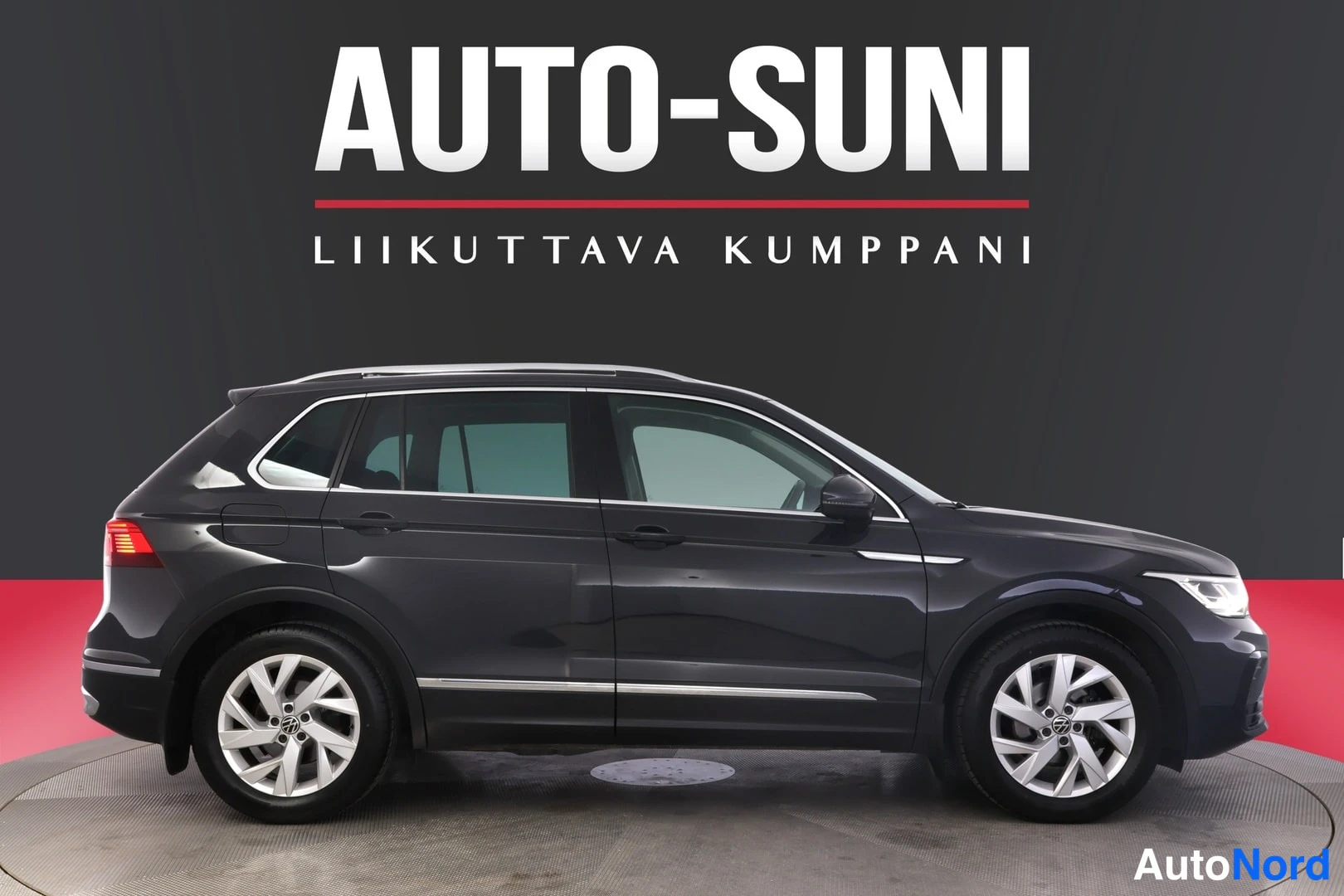 Etuviisto, nokka oikealle: Mustan Volkswagen Tiguanin etukulma kyljestä oikealle, hopeavanteet ja kattokaariet näkyvät.