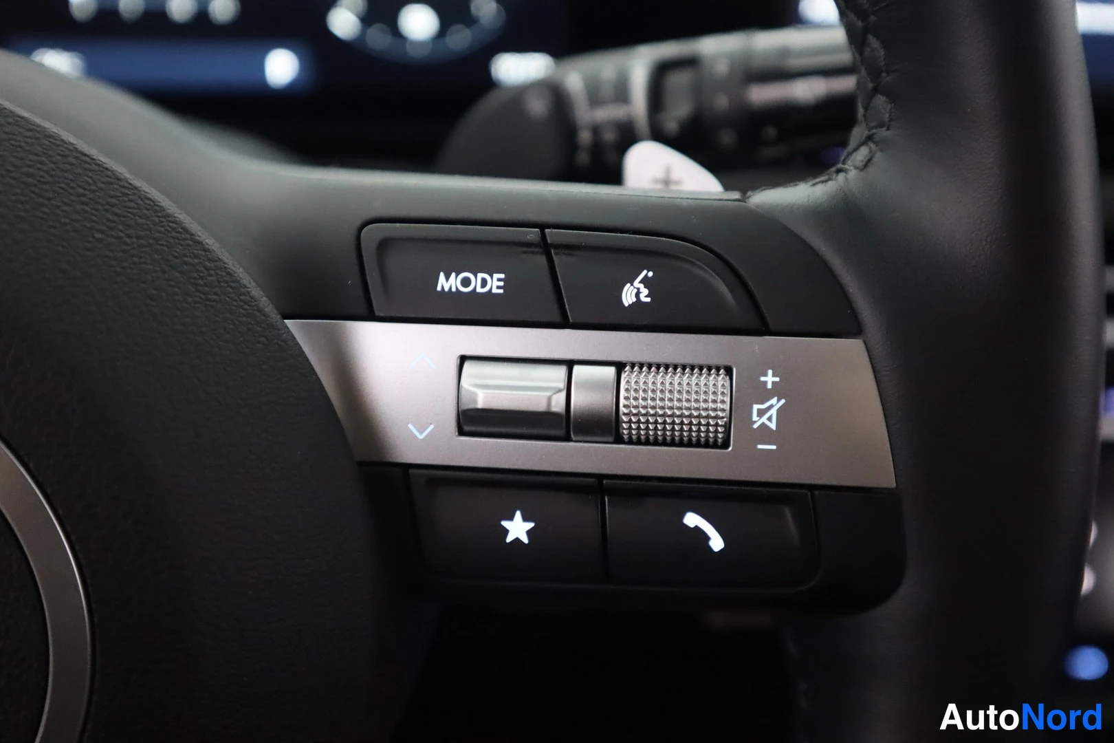 Muu: Lähikuva ohjauspyörän ratissa olevista painikkeista: MODE, äänenvoimakkuuden säädin, selailurulla, tähti- ja puhelinpainike.