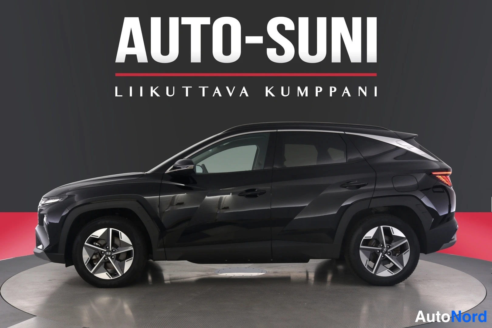 Takaa: Musta maasturi sivusuunnassa studiotauustaa vasten, takavalo ja molemmat pyörät näkyvissä, ylhäällä Auto-Suni-logo.