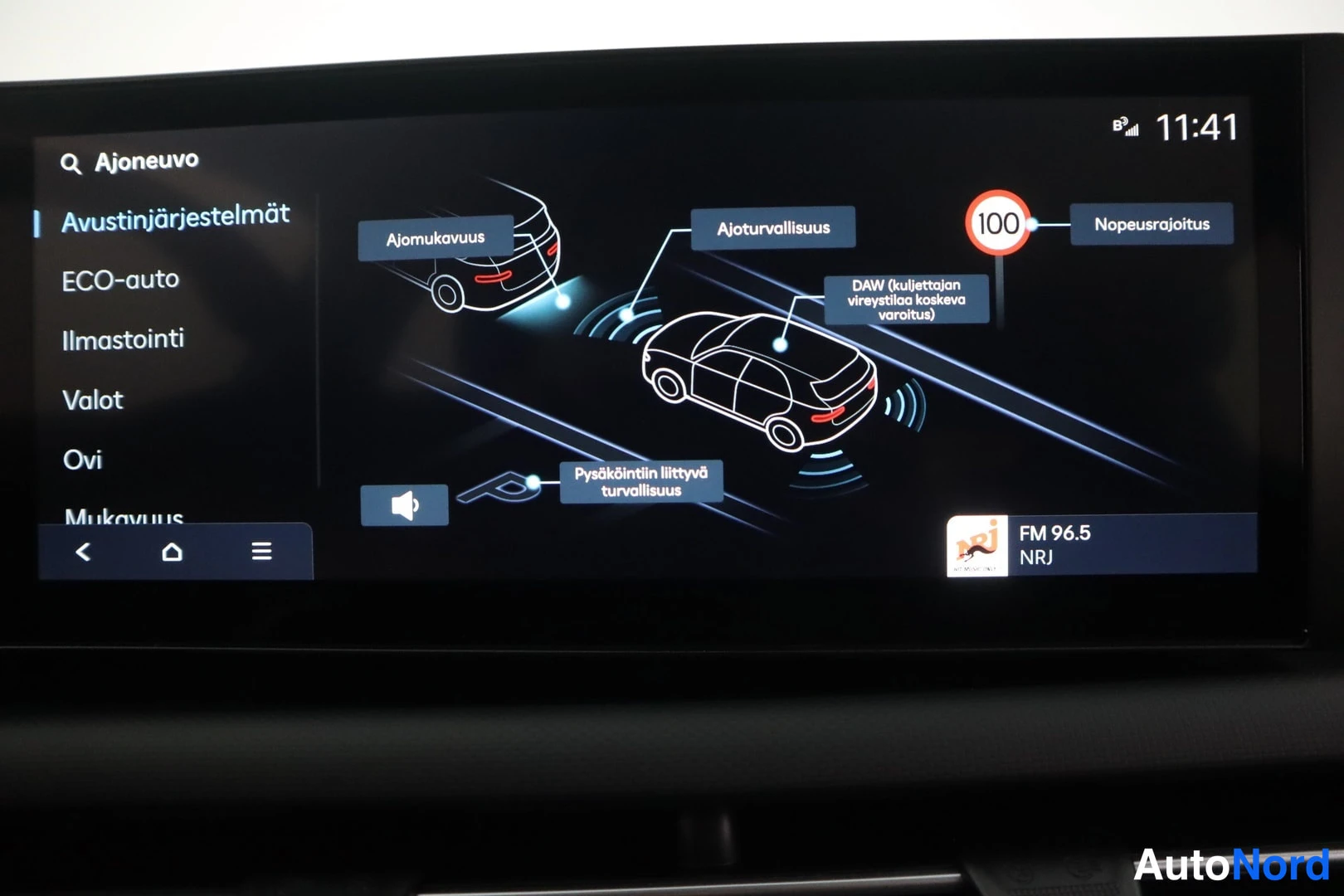 Muu: Auton infotainment-näytön Avustinjärjestelmät-valikko, jossa kuvitteet ajomukavuudesta, ajoturvallisuudesta, pysäköinnistä ja nopeusrajoituksesta 100; kello 11: