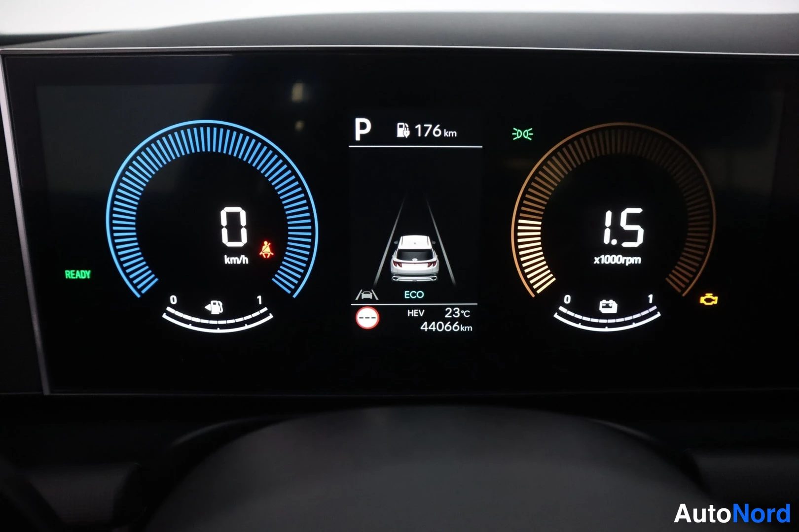 Ohjaamo: Kuva autokunnan mittareiden digitalisesta näyttöstä. Vasemmalla virtalähdemittari osoittaa nollaa km/h ja oikealla kierroslukumittari noin 1500 rpm. Keskellä nä