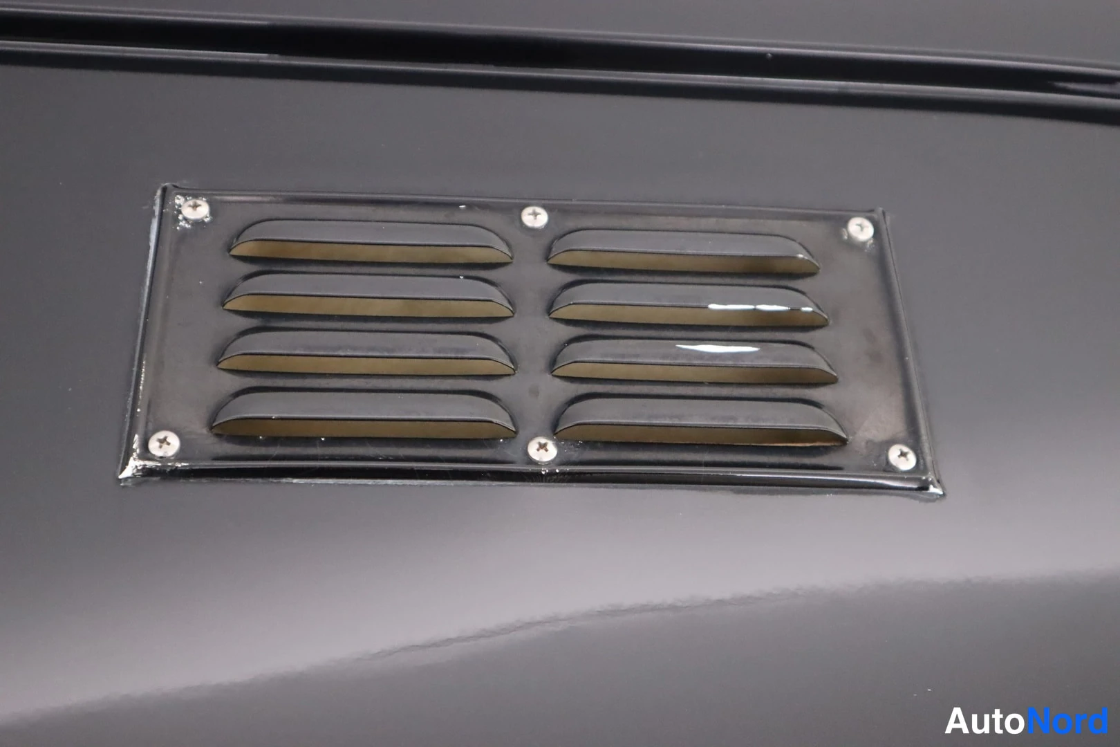 Yksityiskohta: Screwed louvred vent panel on glossy dark bodywork.