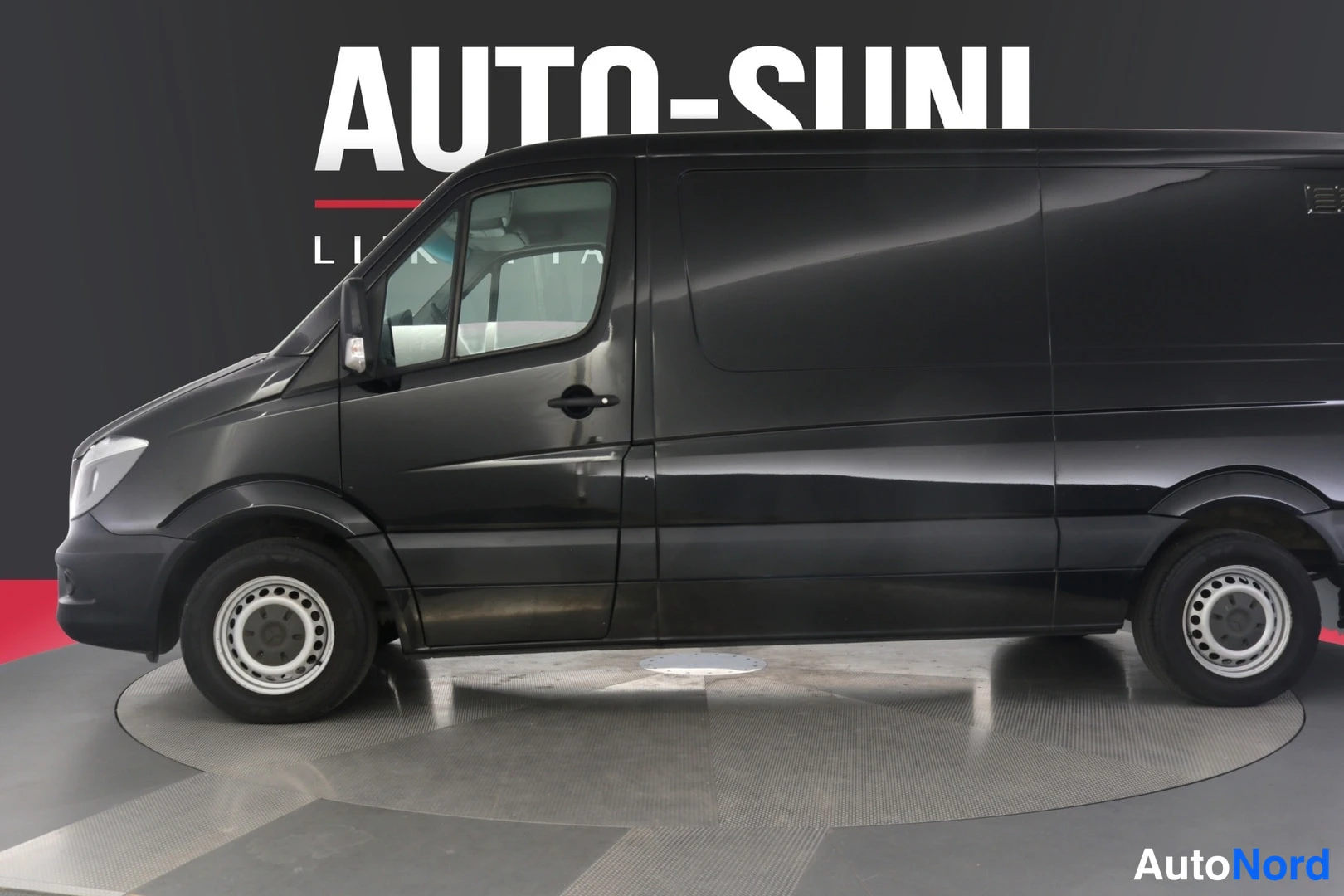 Etuviisto, nokka vasemmalle: Musta Mercedes-Benz Sprinter -pakettiauto etukulmasta, AAMUHEI-KILPAILUKUVA taustallaAuto-Suni-tekstillä.