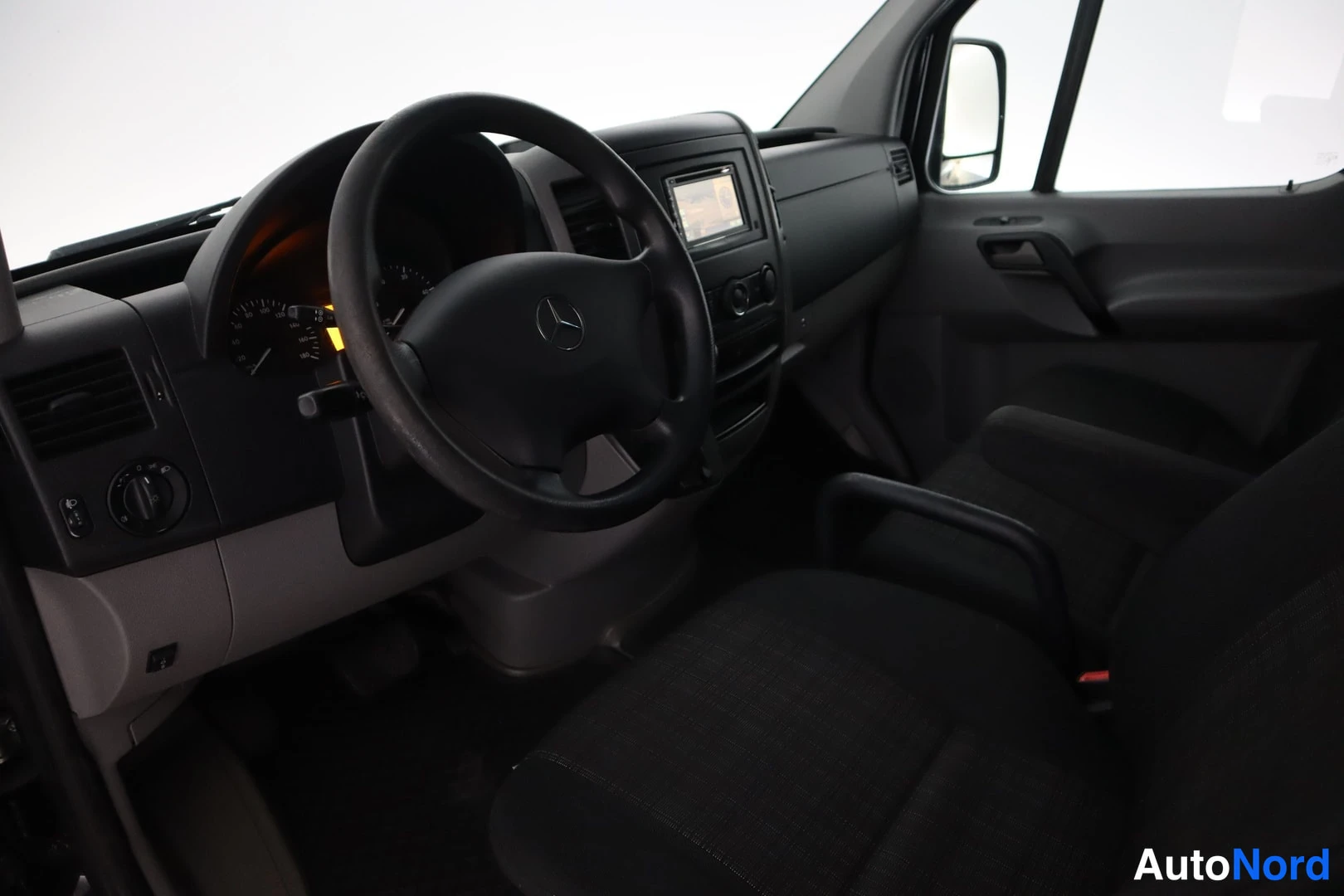 Takaviisto: Mercedes-Benz Sprinterin ohjaamo: ratit, kojelauta, radiolaite ja tummat istuimet.