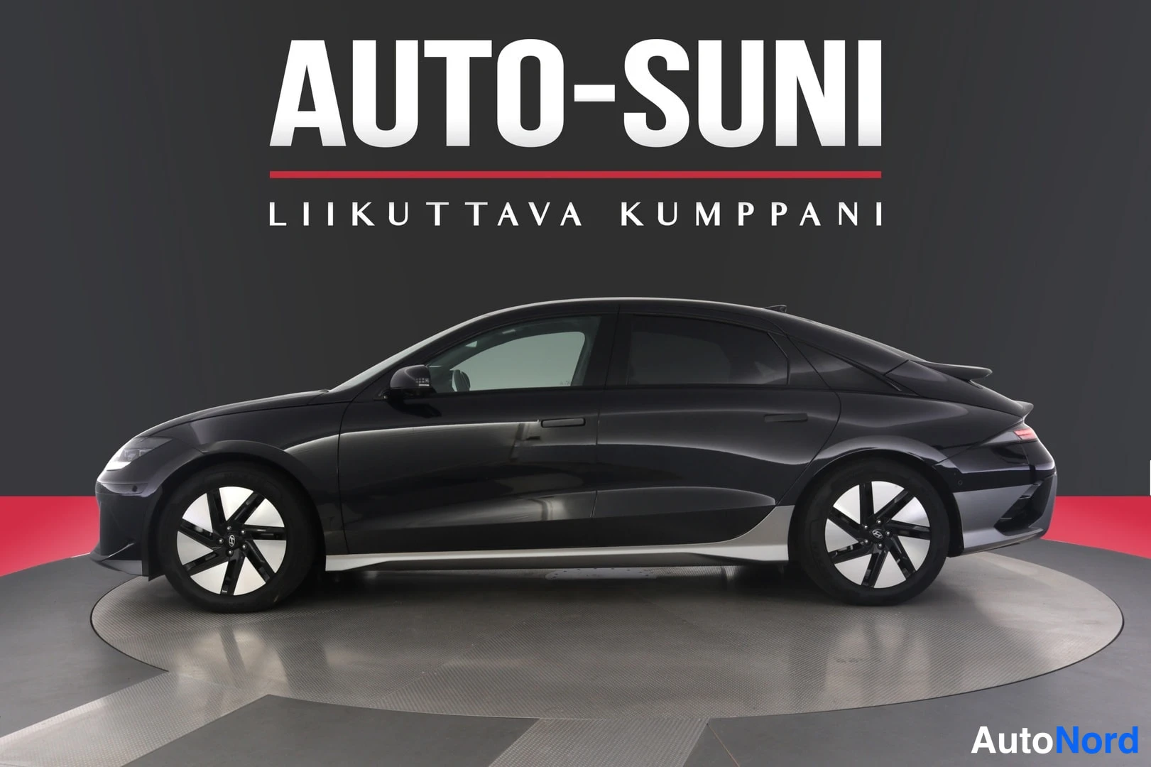 Sivulta: Full side profile view of a black sedan parked on a circular platform with 'AUTO-SUNI' text in background