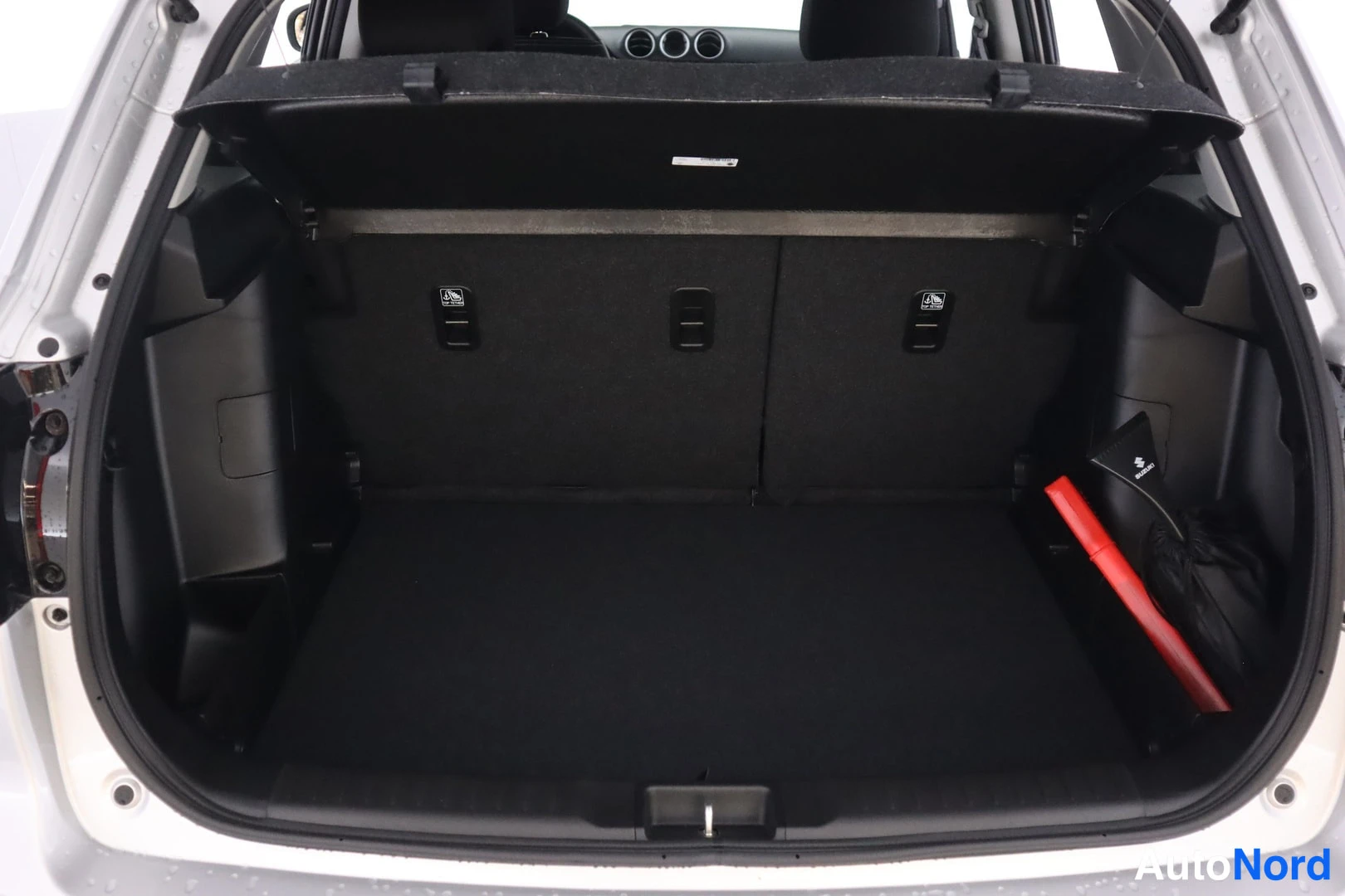Tavaratila: Avattu tavaratila mustalla matolla, takaselustan Isofix-merkinnät ja tavaratilan oikealla reunassa punainen varoituskolmio ja musta puska.