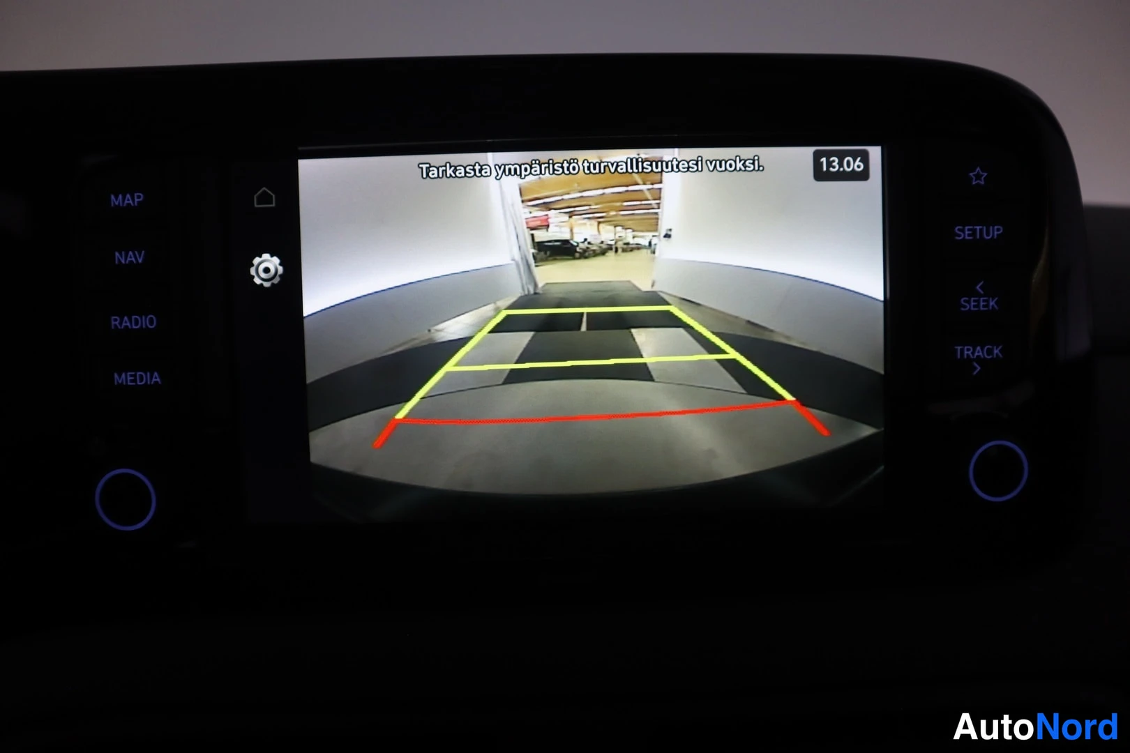 Muu: The central infotainment display shows the rear-view camera feed with parking guidelines and a warning text in Finnish: 'Tarkasta ympäristö turvallisuutesi vuok