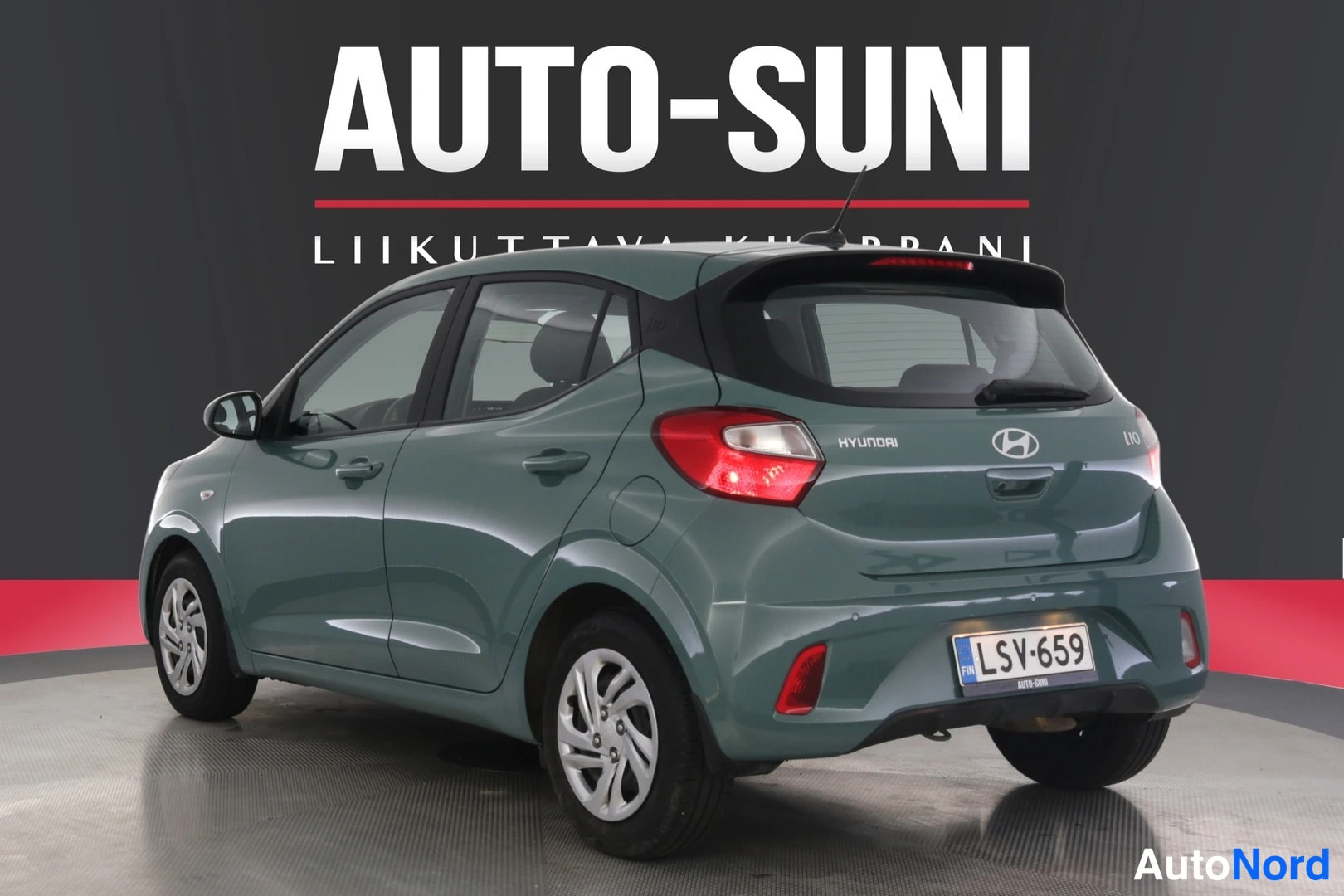 Takaviisto: Kuva Hyundai i10:stä mustasta reunusvarustetusta tavaratilasta, jossa on lattiaversiot. Takapäässä näkyy taustavalot, Hyundai-logo ja rekisterinumero.