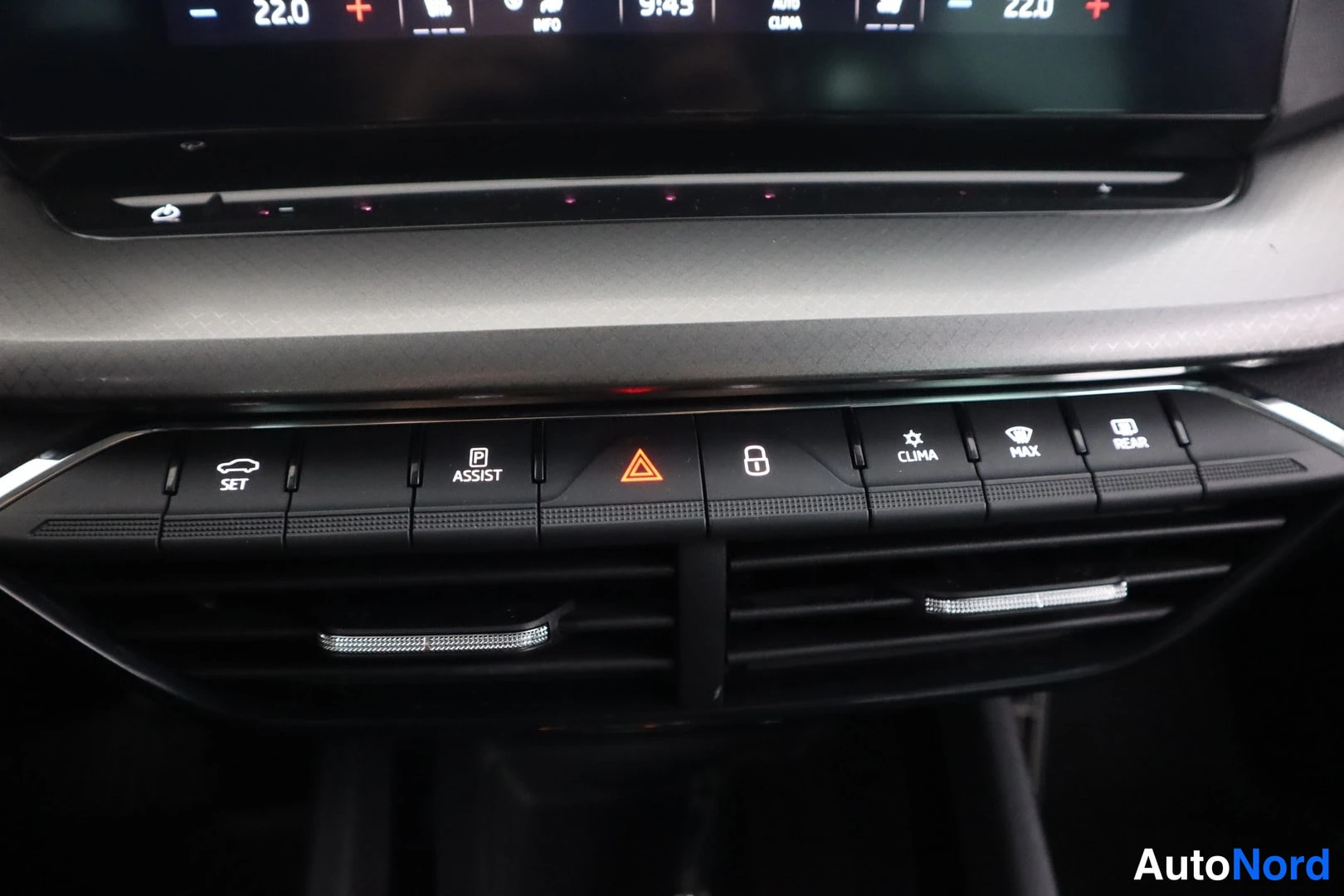 Yksityiskohta: Close-up photo of the car's center console control panel below the infotainment screen. Visible are a button for parking sensors (SET), traction control or stab