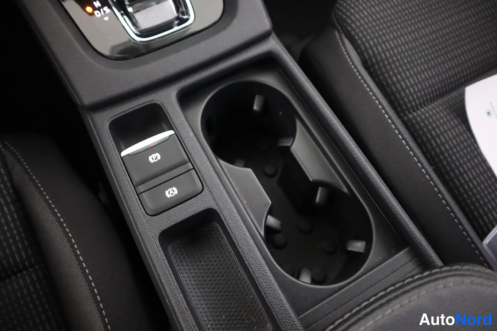 Yksityiskohta: Detail of the center console between the front seats. The image shows an electric parking brake switch with a red ring and an auto-hold function button below it