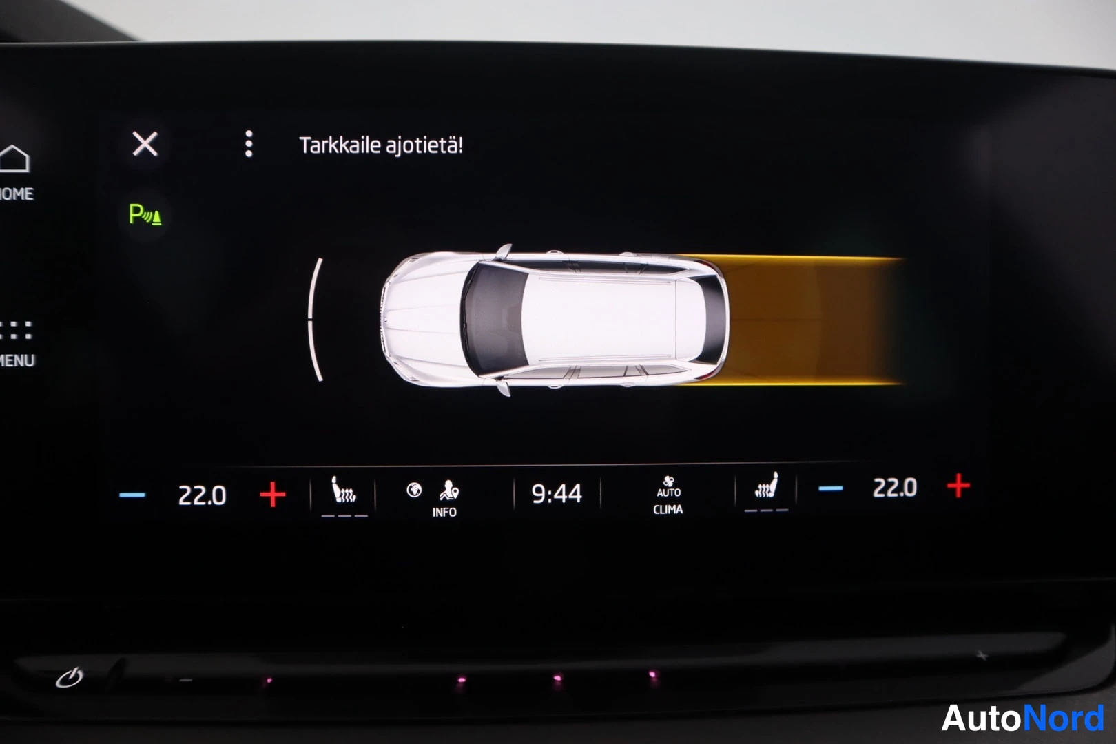 Yksityiskohta: Infotainment-näytöllä pysäköintianturien näkymä, teksti 'Tarkkaile ajotietä', molempien puolien lämpötila 22,0 astetta ja kello 9:44.