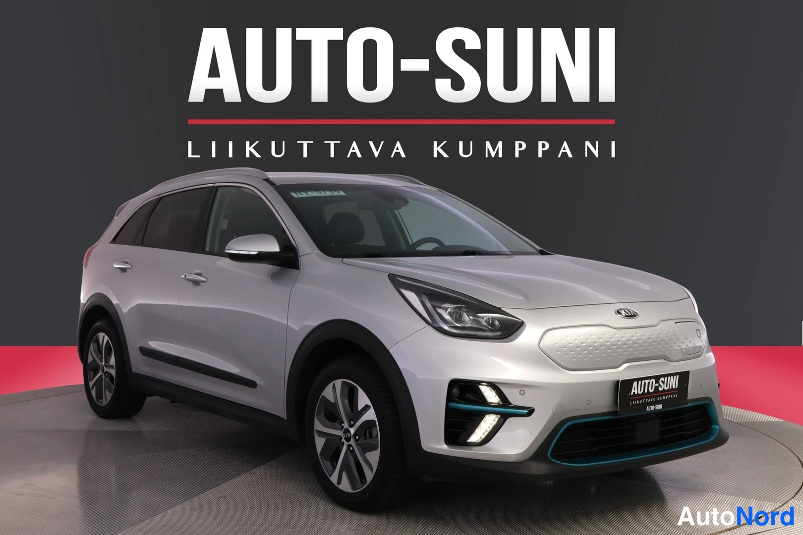 Etuviisto, nokka oikealle: Kia Niro e-SUV, etuviisto oikealta, hopeinen koriratkaisu, LED-ajovalot ja Auto-Suni-mainoskyltti.