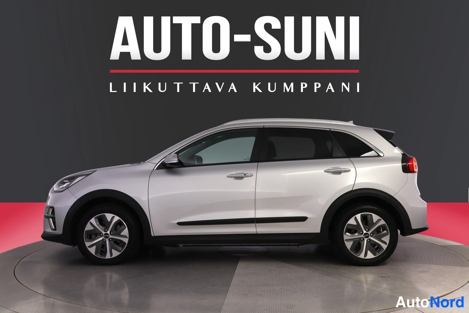 Etuviisto, nokka vasemmalle: Hopeinen Kia Niro sivulta kuvattuna merkin myyntihallissa.