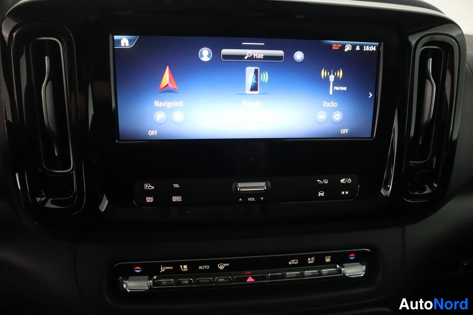 Yksityiskohta: Auton kojelaudan keskirivi: taktiilinen näyttö, jossa päävalikko Navigointi, Puhelin ja Radio, sekä alla ilmastointipaneeli AUTO- ja A/C-merkinöillä.