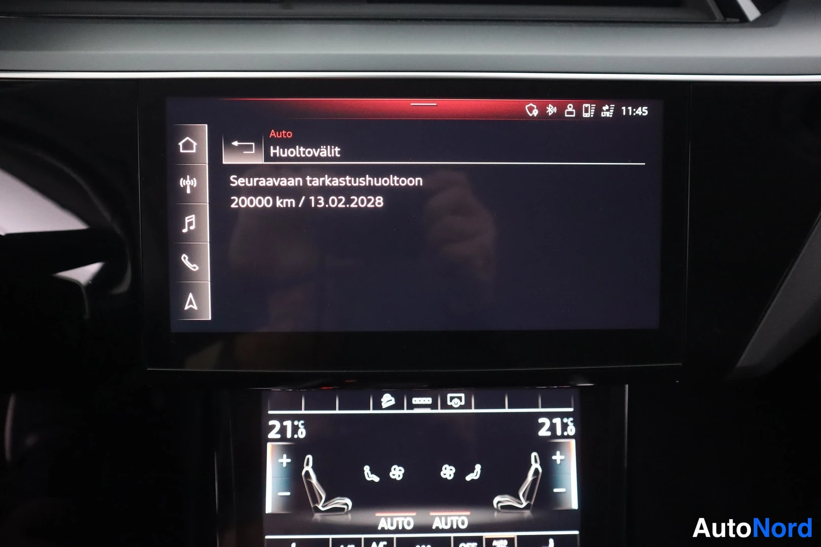 Yksityiskohta: Keskikäyttöpaneelin näyttö huoltovälien tiedot: seuraava tarkastushuolto 20000 km / 13.02.2028. Alla ilmastointipaneeli, lämpötila 21,0 astetta.