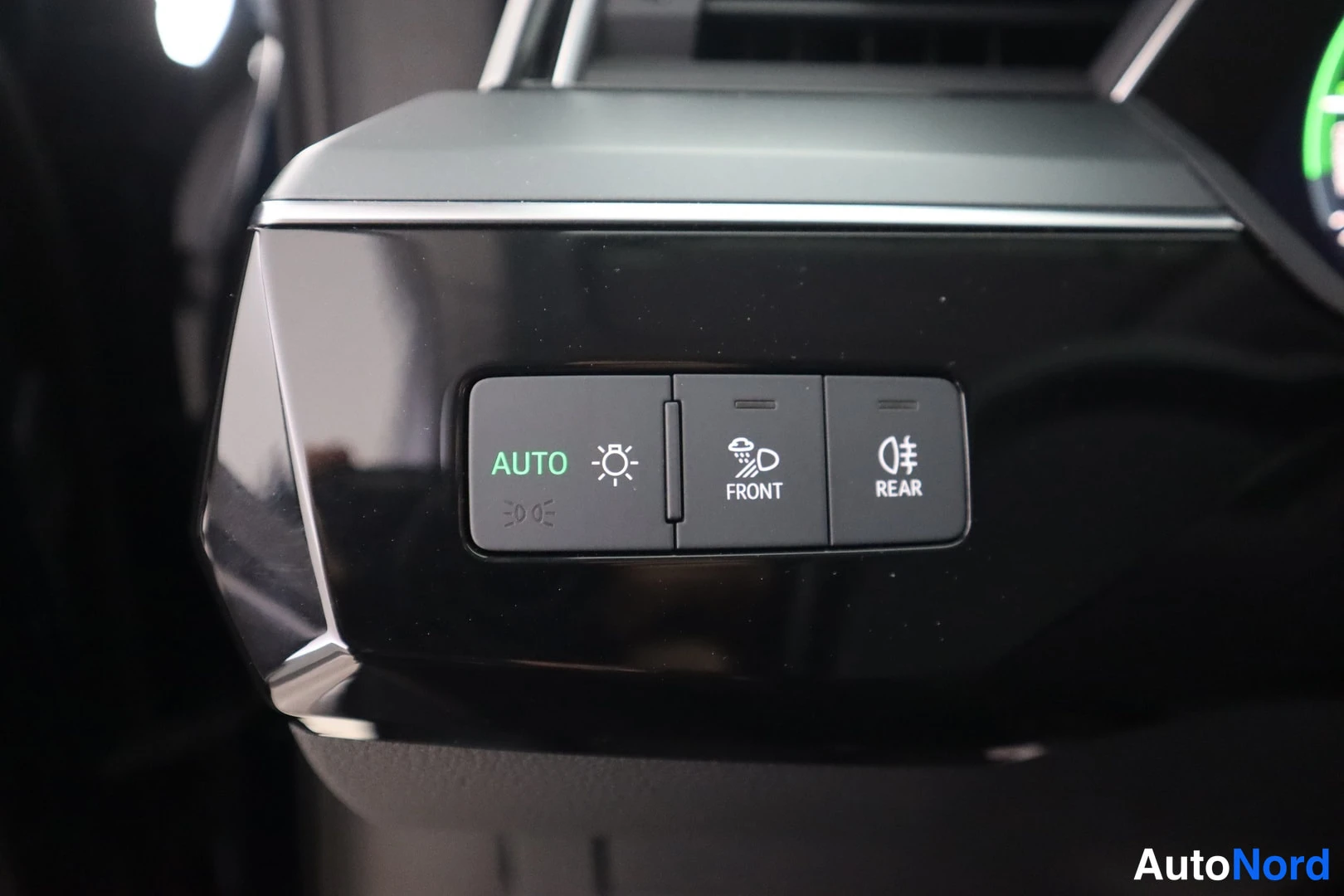 Muu: Lähikuva kojelaudan napeista: AUTO-valo kytkettynä, sumuvalo FRONT ja REAR; paneelin ympäristö on musta, kiiltävä.