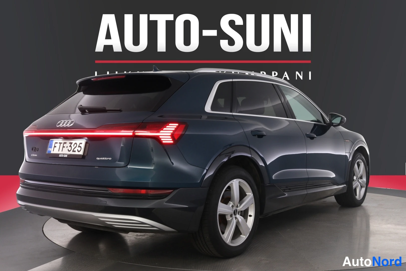 Takaviisto: Tummansininen Audi e-tron -maasturi kuvattu takaa kulmasta, takavalojen valotunnus päällä, rekisterikilpi.