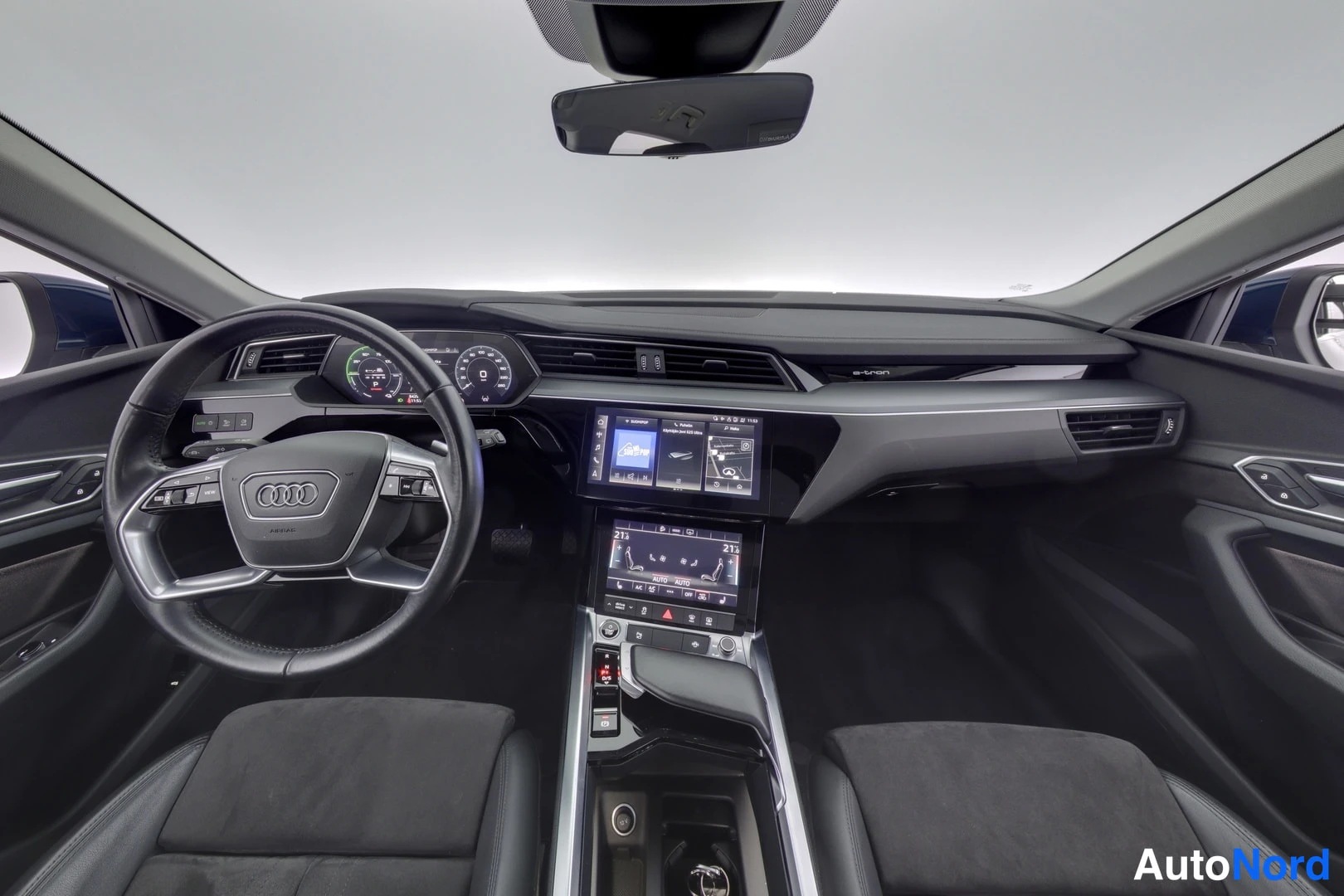 Muu: Audi e-tronin ohjaamo edestäpäin: ohjauspyörä, digitaalinen mittaristo ja kaksi keskikonsolin kosketusnäyttöä, mustat istuimet.