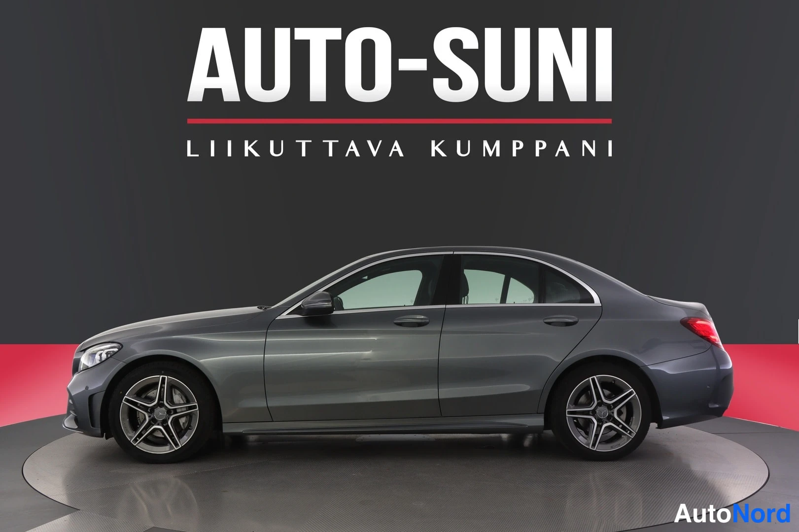 Sivulta: Harmaa Mercedes-Benz-sedan kylki- ja etukulmassa tummalla taustalla, etusäleikkö vasemmalla.