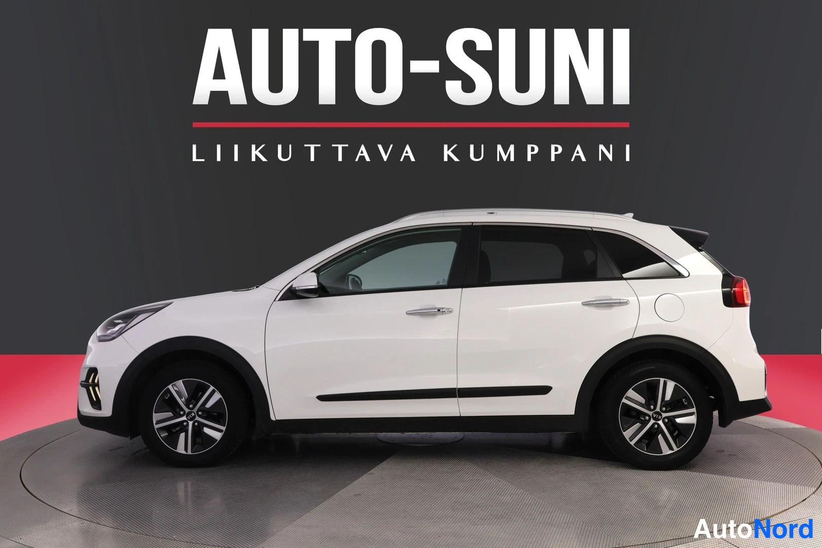 Sivulta: Valkoinen Kia Niro -farmuriajooninen auton sivukuva, kylki ja molemmat pyörät näkyvissä studioseinämää vasten, Autosuni-logo taustalla.