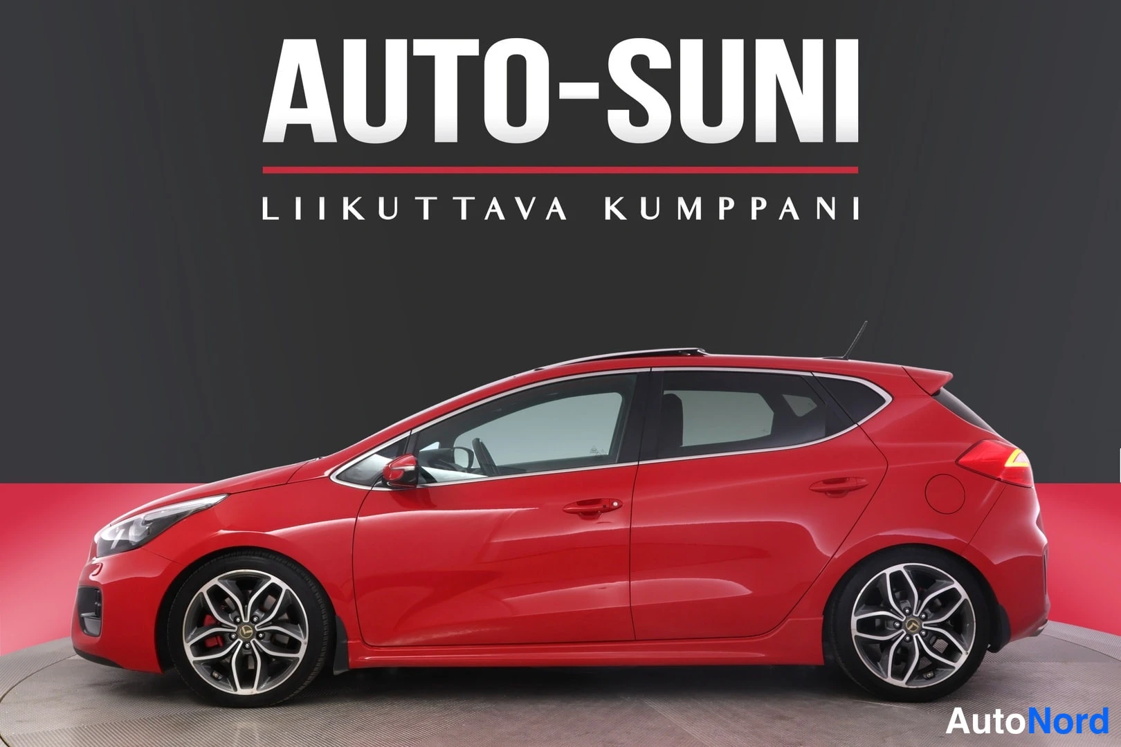 Sivulta: Punainen Kia Ceed viistosti edestä vasemmalta kuvattuna studioympäristössä, AUTO-SUNI-mainosteksti taustalla.
