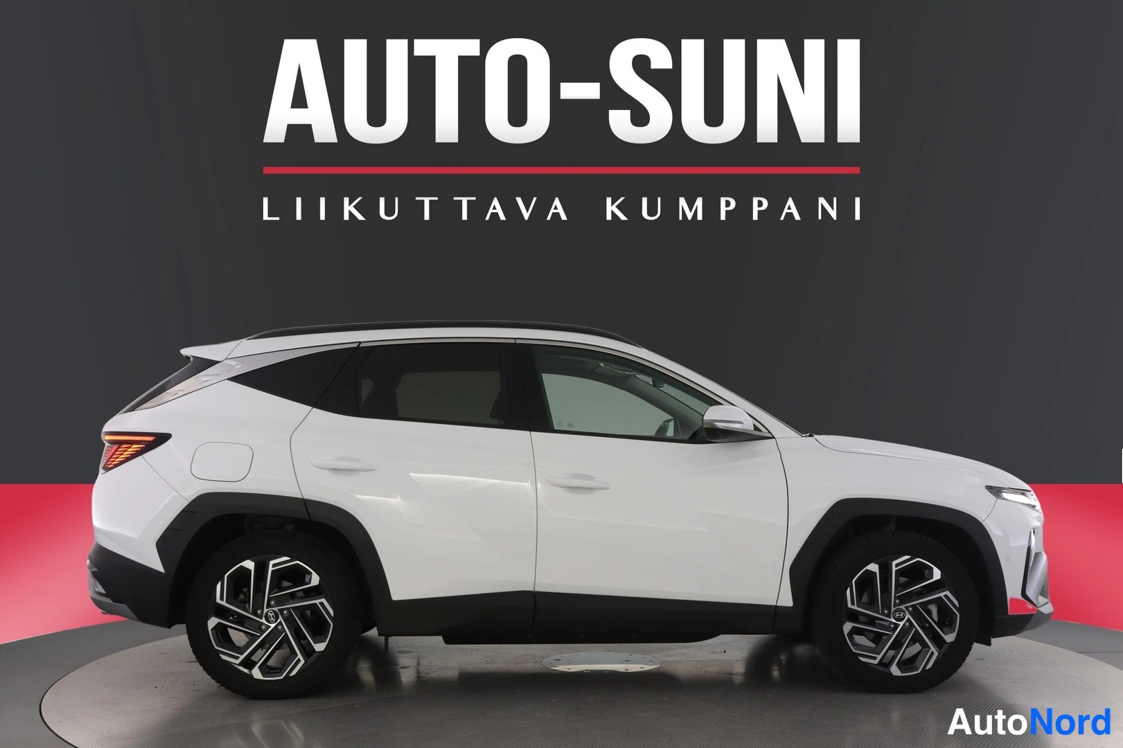 Sivulta: Hyundai Tucson, valkoinen auto sivulta kuvattuna, näkyvät takavalot ja pyörät, studiotausta Auto-Suni-logo
