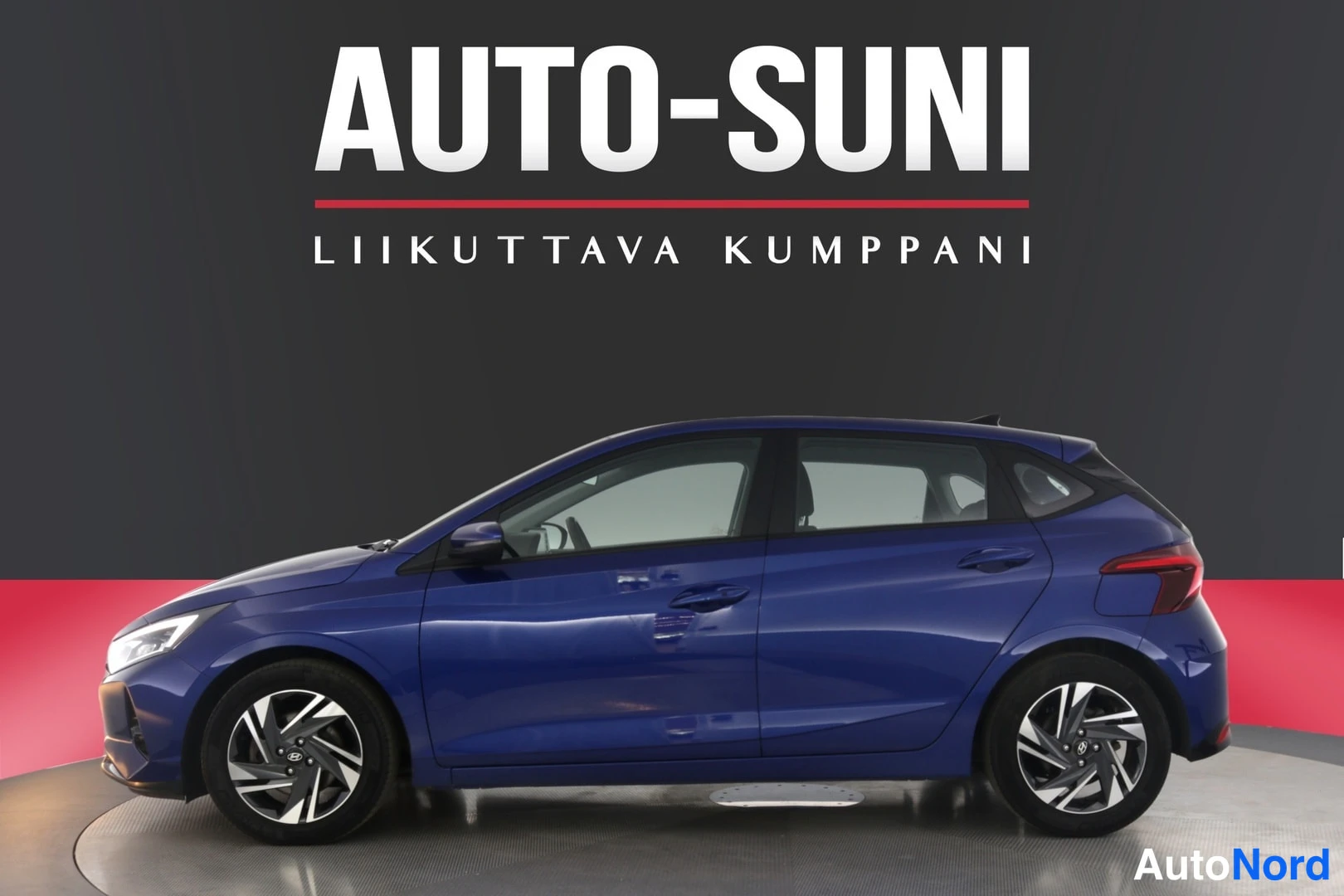Sivulta: Sininen viisiovinen Hyundai i20 -henkilöauto sivusta valokuvastudion tummalla taustalla.