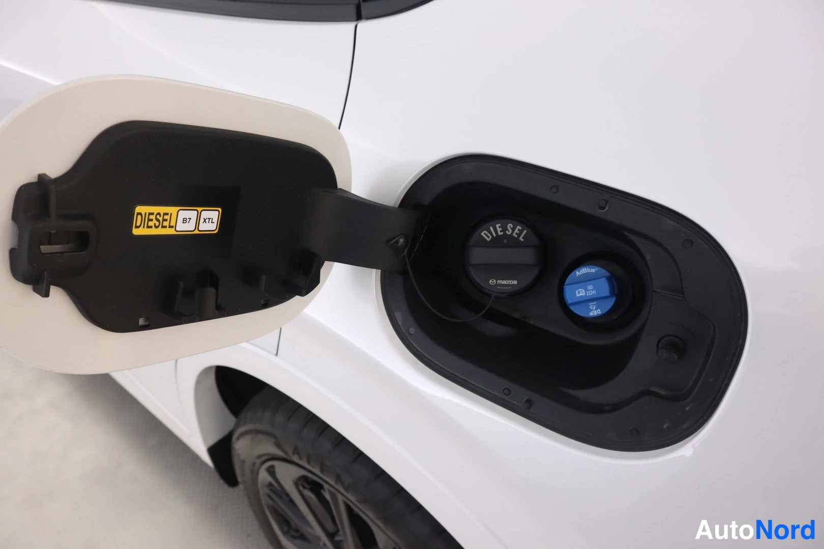 Edestä: Sisäkuva polttoainesuukun kannen alta: DIESEL B7 XTL -tunnisteinen korkki ja bensiinin täyttöaukko.