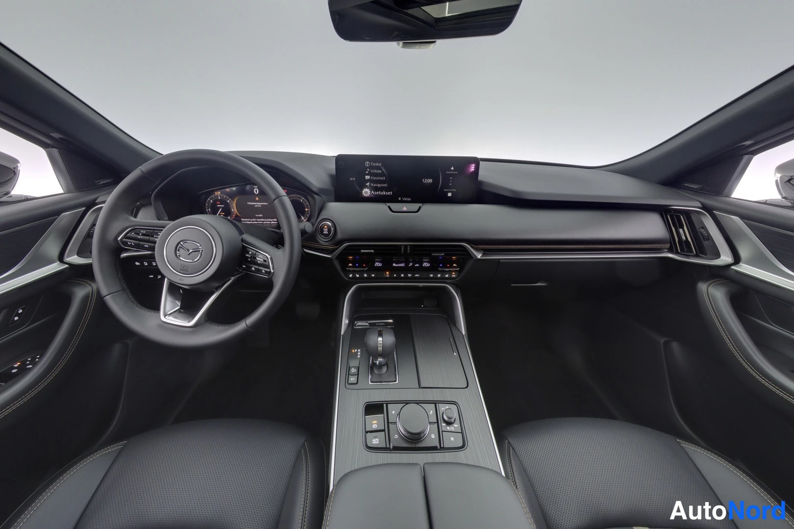 Muu: Mazda CX-60:n kojelauta ja ohjauspyörä mustalla nahkaverhoilulla, keskinäyttö ja keskikäytävän vaihdevalitsija näkyvät.