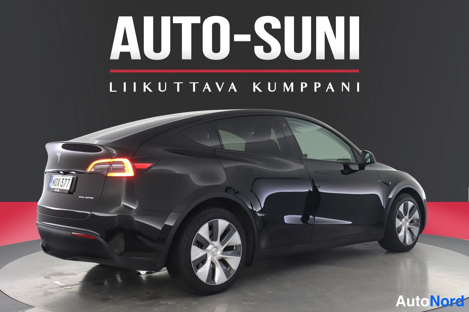 Takaviisto: Musta Tesla Model Y takaosa ja vasen kylki näkyvät, takavalot syttyneinä, rekisteritunnus.