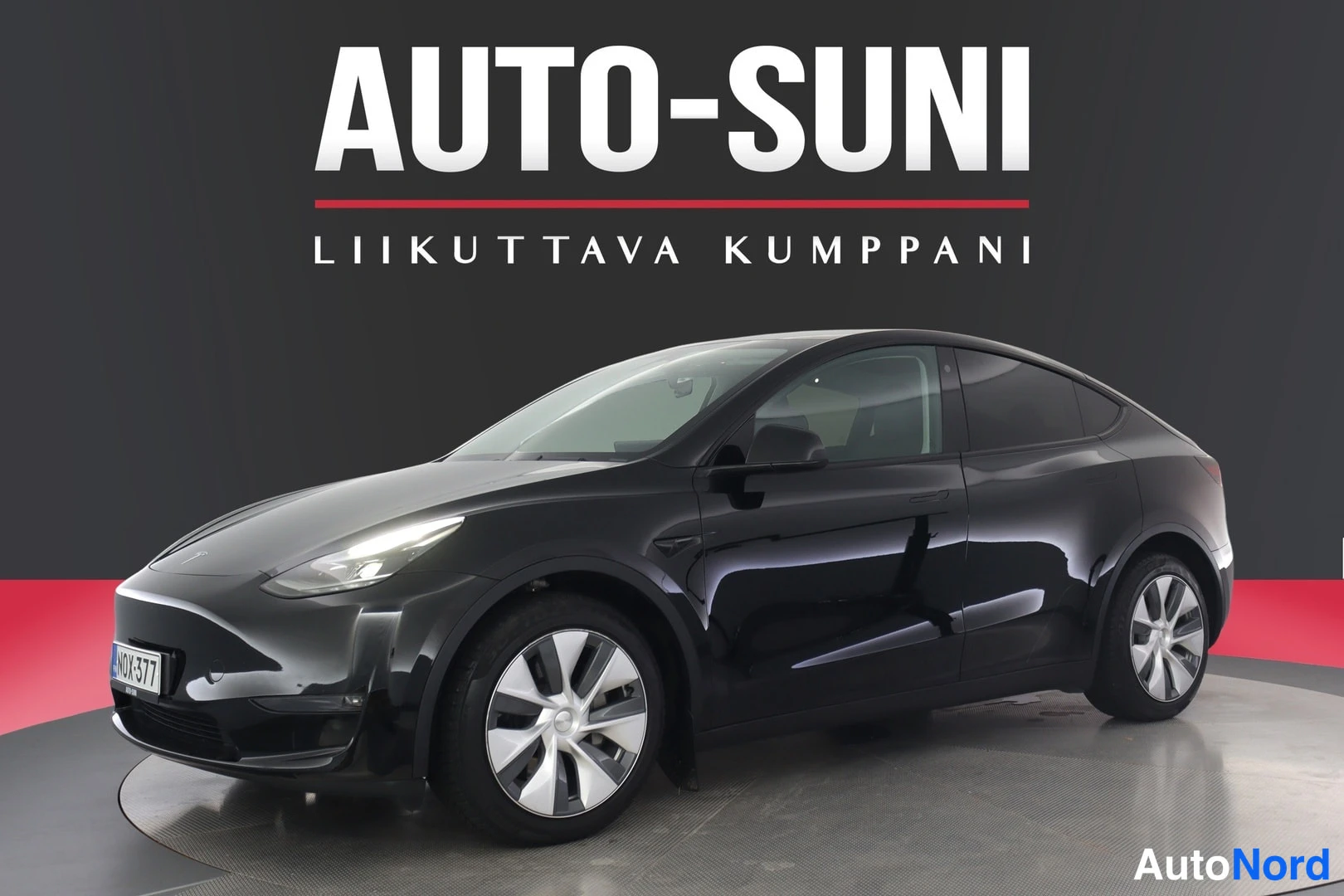 Etuviisto, nokka vasemmalle: Mustan henkilöautin etukolmikkonäyttö vasemmalta edessä, logo ja rekisteritunnus näkyvät.