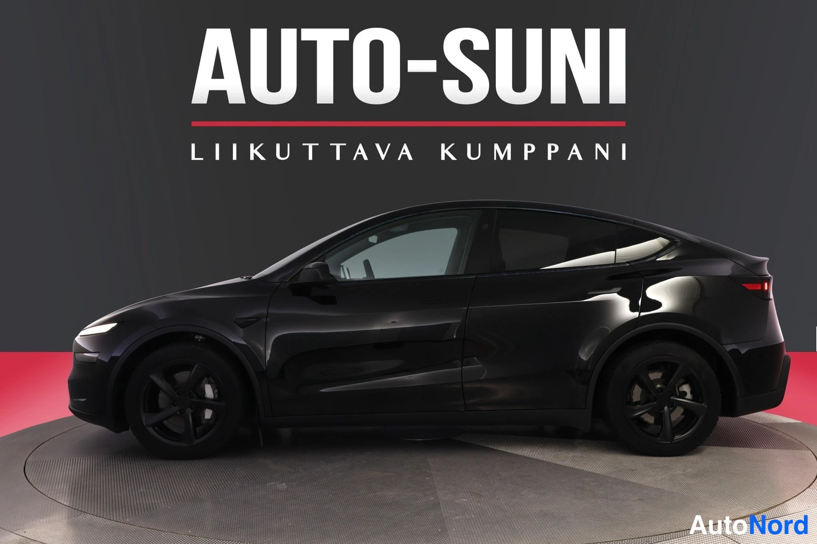 Etuviisto, nokka vasemmalle: Musta Tesla Model Y sivusta vasemmasta etukulmasta, keulakivi ja etupyörä näkyvät kuvan vasemmassa reunassa.